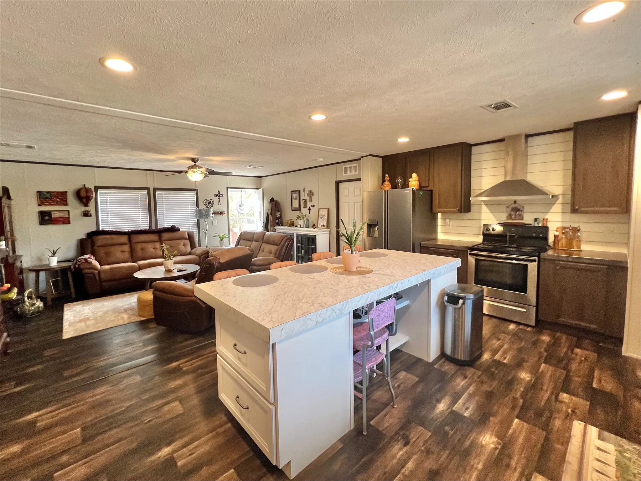 Kitchen featuring recessed lighting, appliances with stainless steel finishes, a breakfast bar area, wall chimney range hood, and light countertops