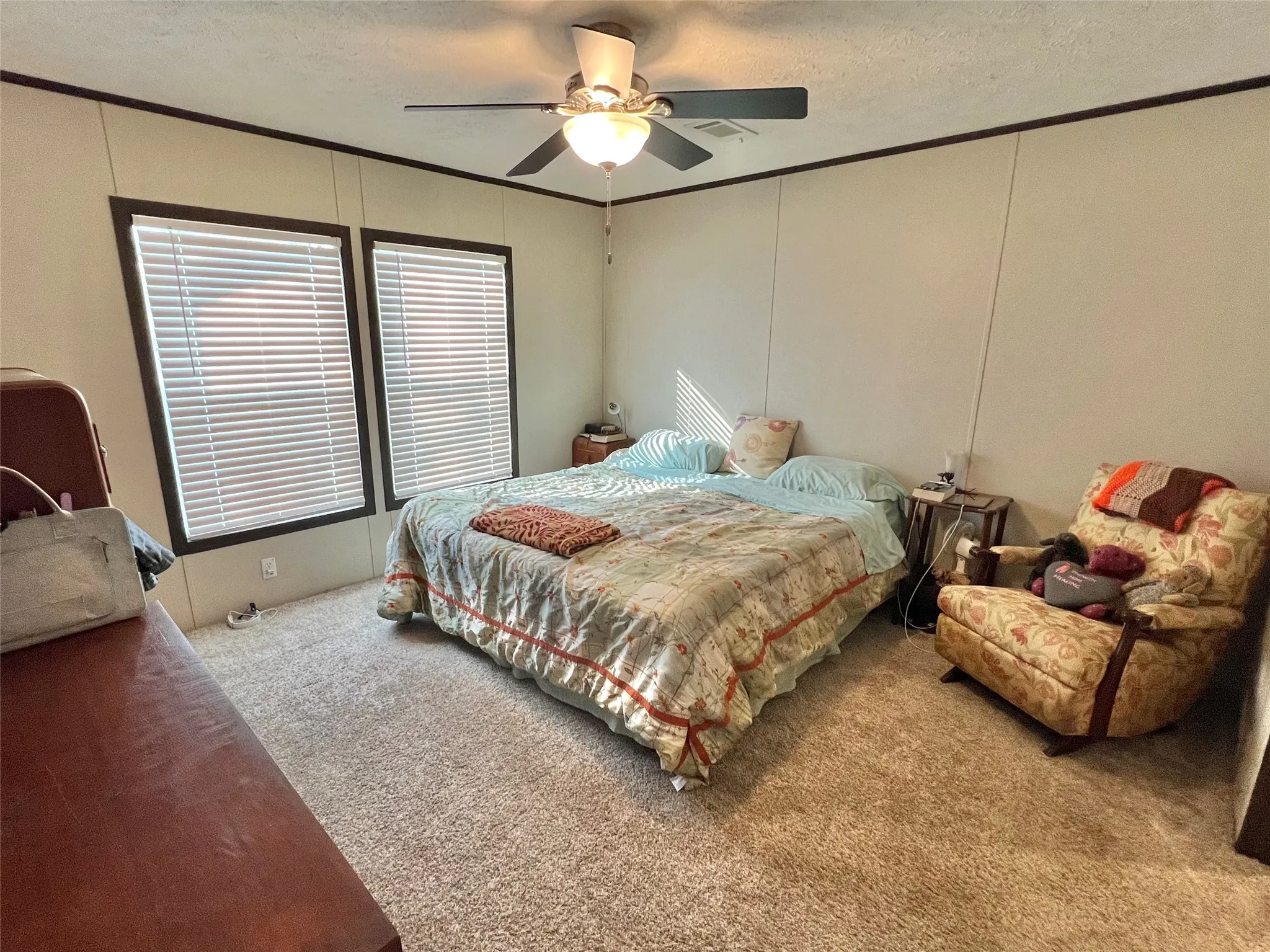 Carpeted bedroom with a textured ceiling, ceiling fan, ornamental molding, and a decorative wall
