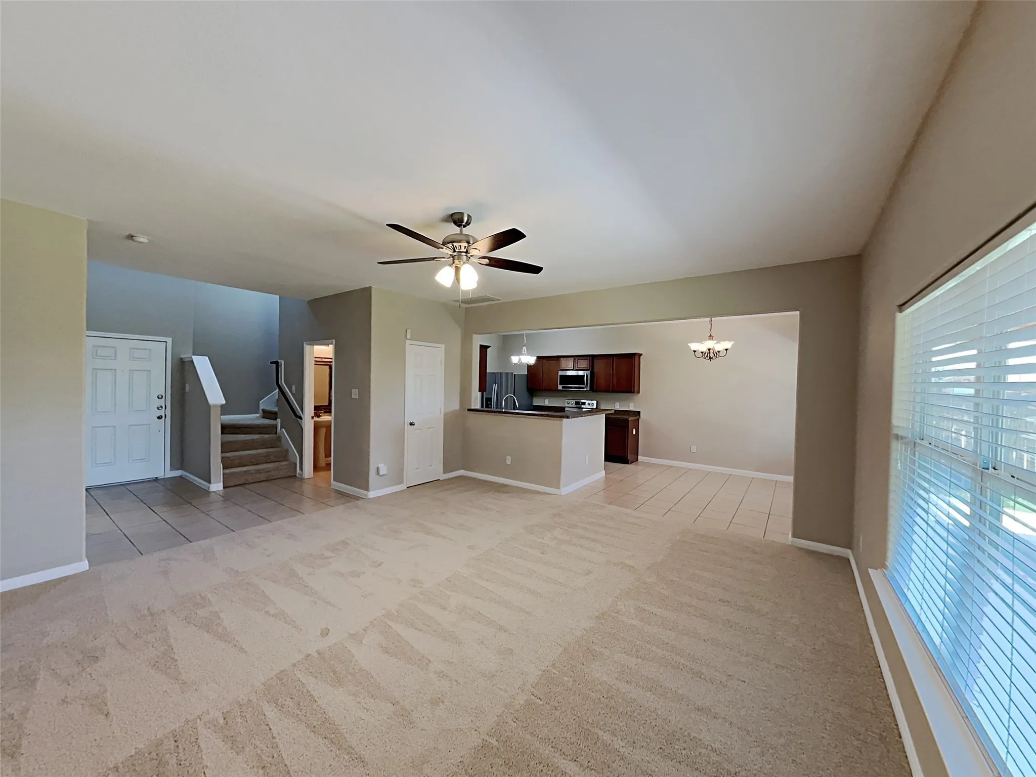 Unfurnished living room featuring stairway, a chandelier, light tile patterned floors, light carpet, and a ceiling fan
