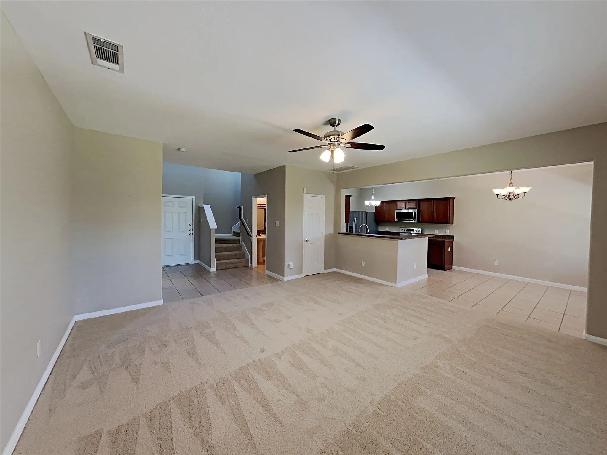 Unfurnished living room with a chandelier, stairs, ceiling fan, and light tile patterned flooring