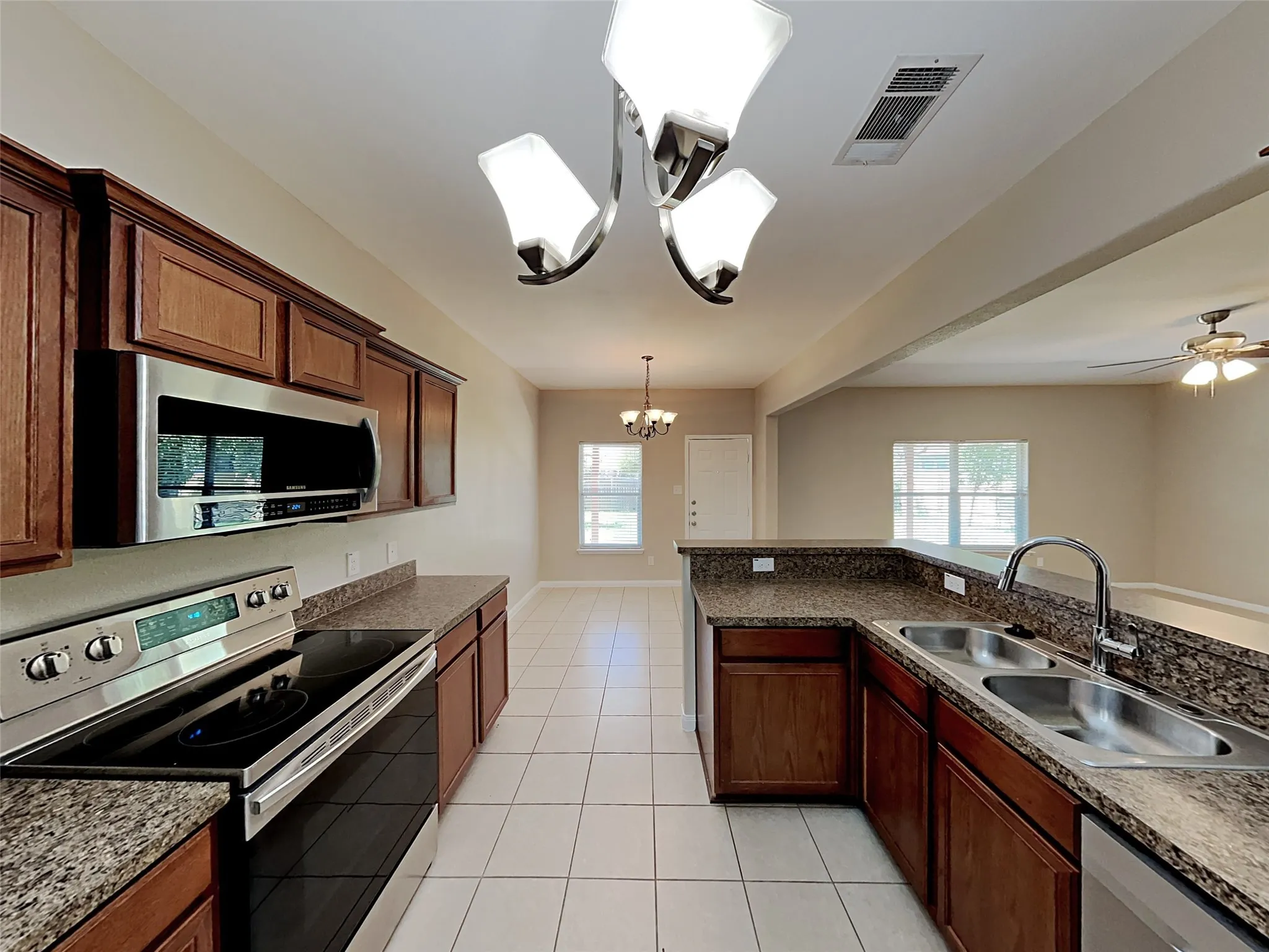 Kitchen featuring stainless steel appliances, hanging light fixtures, light tile patterned floors, a chandelier, and healthy amount of natural light