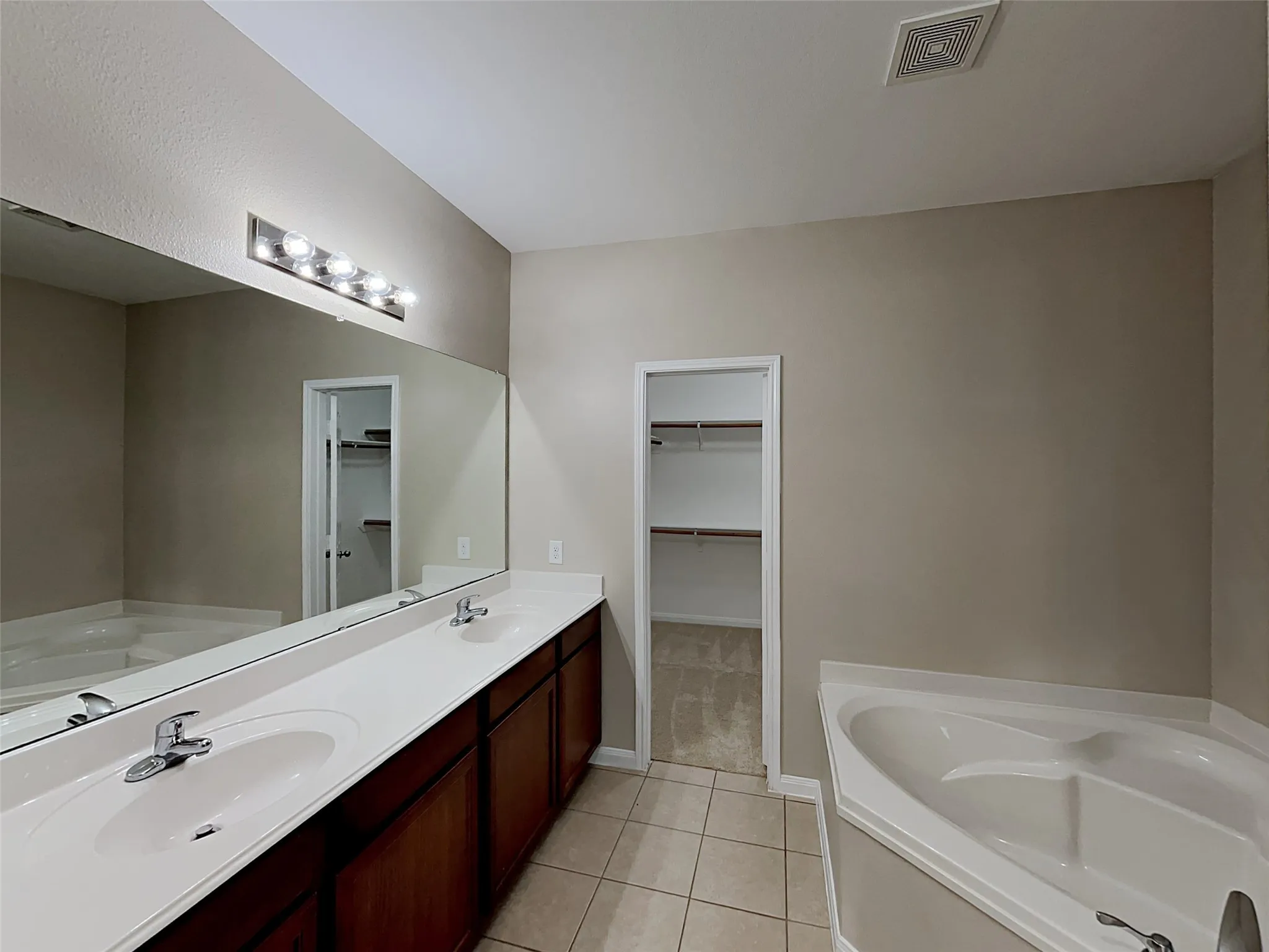 Bathroom featuring a garden tub, a spacious closet, double vanity, and light tile patterned floors