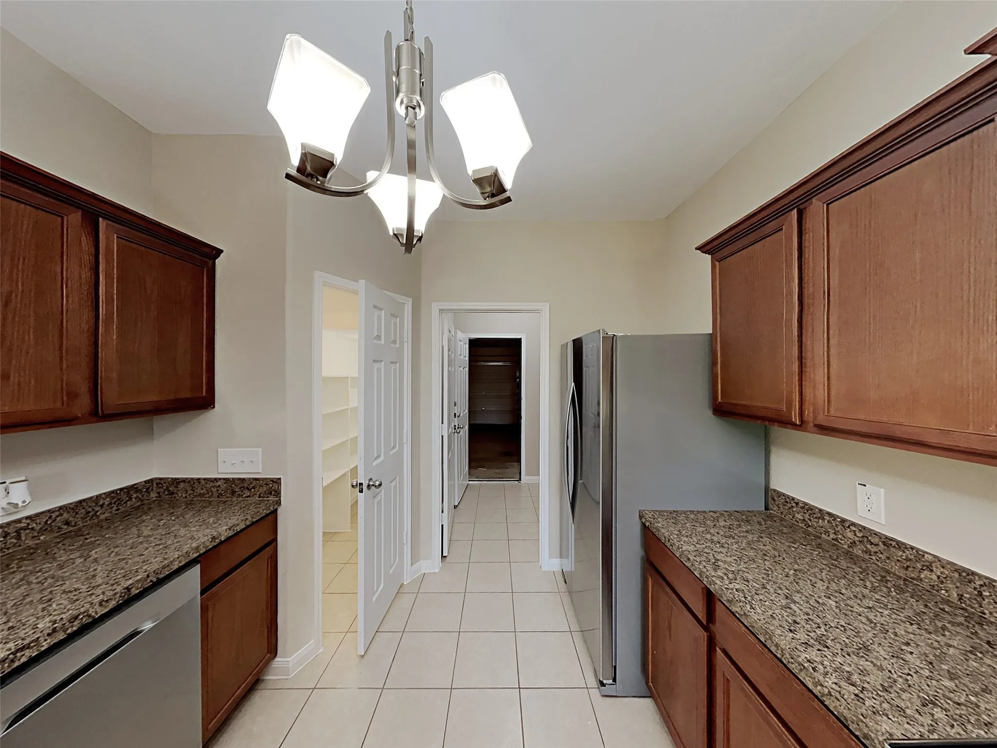 Kitchen featuring stainless steel appliances, hanging light fixtures, dark stone counters, and light tile patterned flooring