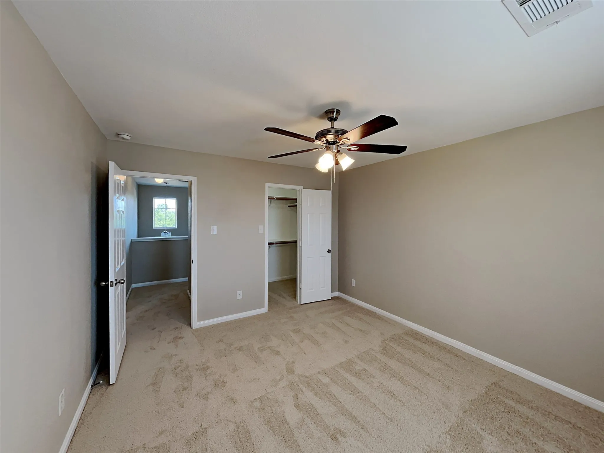 Unfurnished bedroom with a spacious closet, light colored carpet, and a ceiling fan