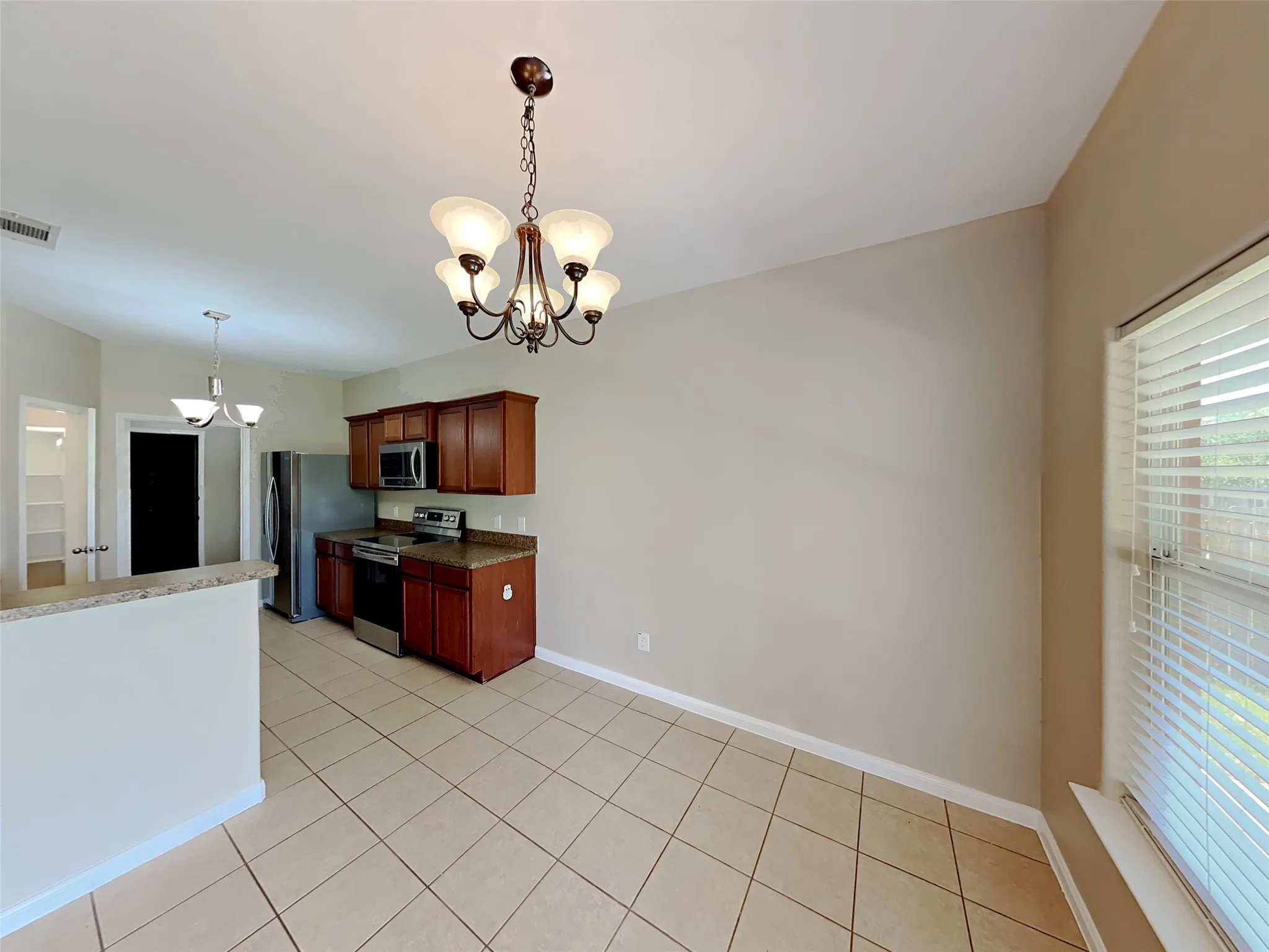Kitchen with a chandelier, appliances with stainless steel finishes, pendant lighting, light tile patterned floors, and dark stone counters