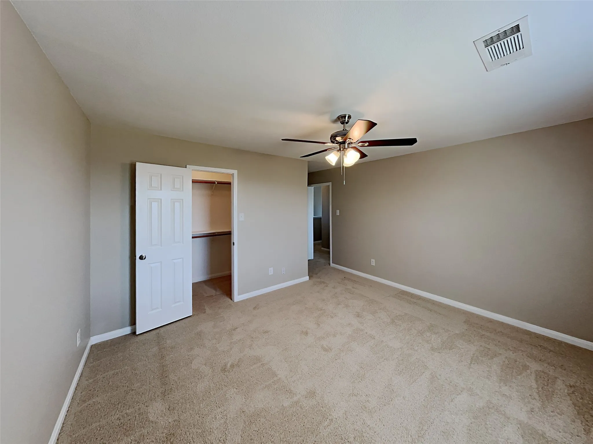 Unfurnished bedroom with a spacious closet, light colored carpet, and ceiling fan