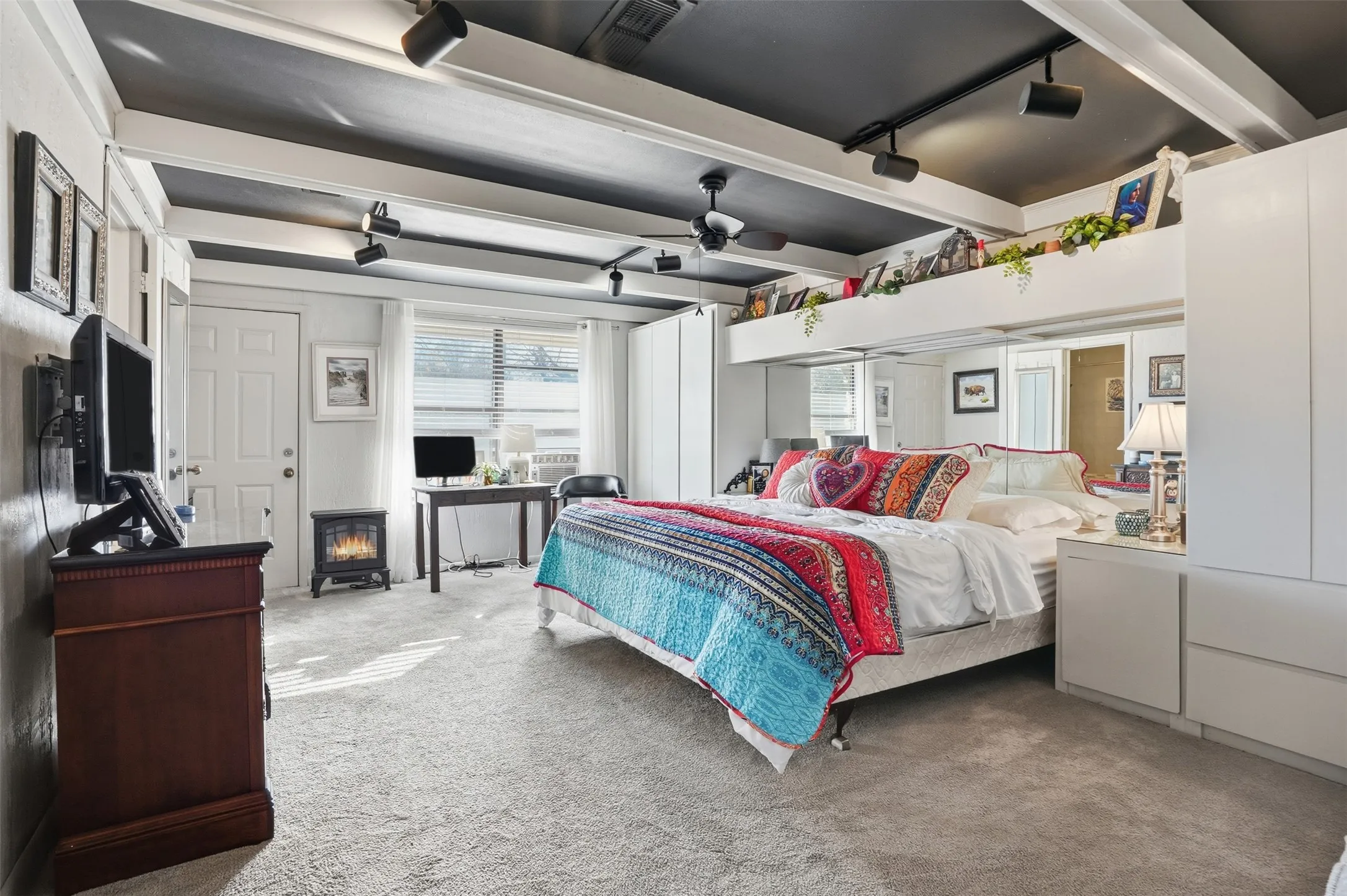 Bedroom featuring carpet floors, beam ceiling, a wood stove, and track lighting