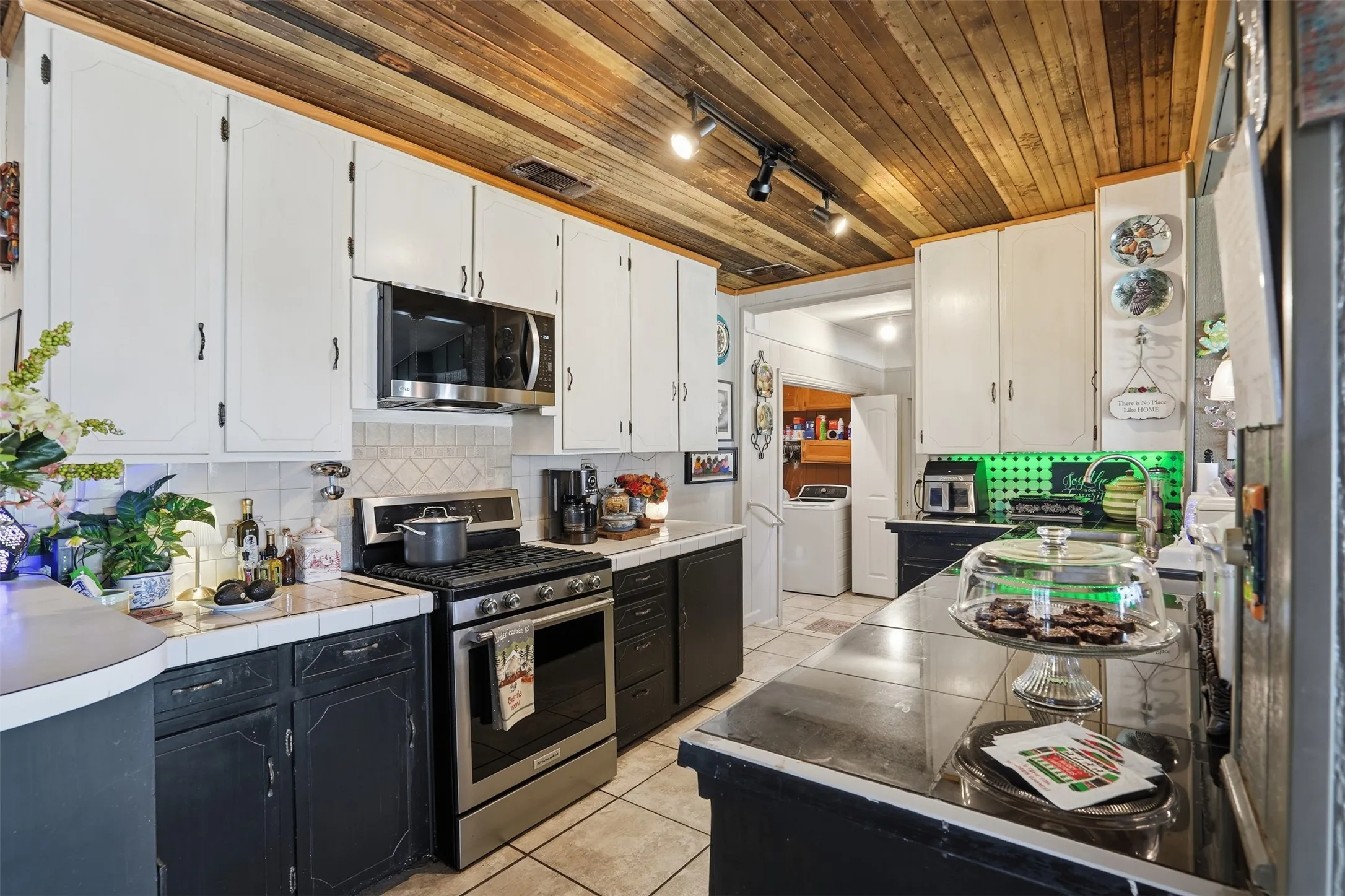 Kitchen featuring wood ceiling, stainless steel appliances, white cabinets, tile counters, and track lighting