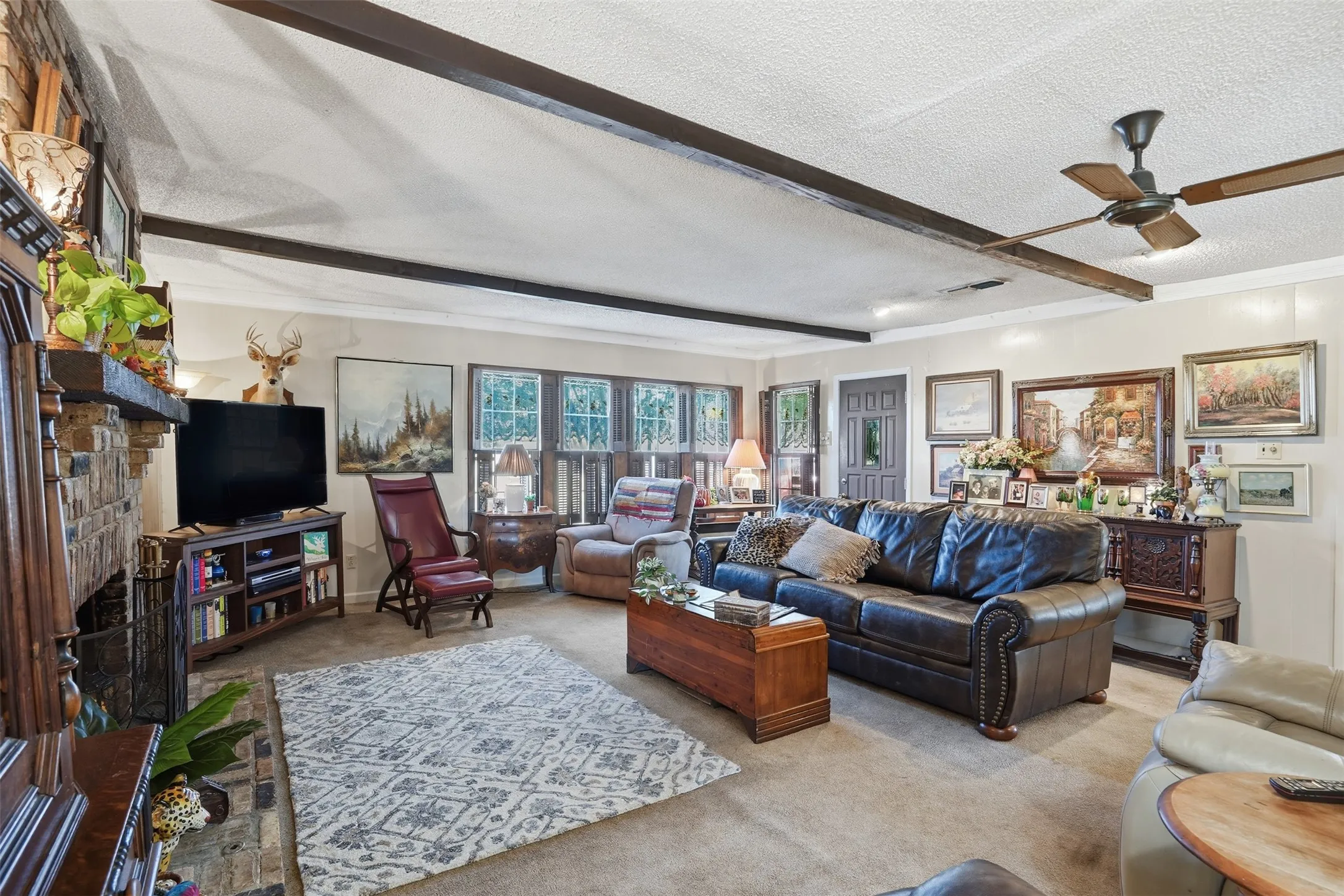 Carpeted living room featuring beamed ceiling, a fireplace, a ceiling fan, and a textured ceiling
