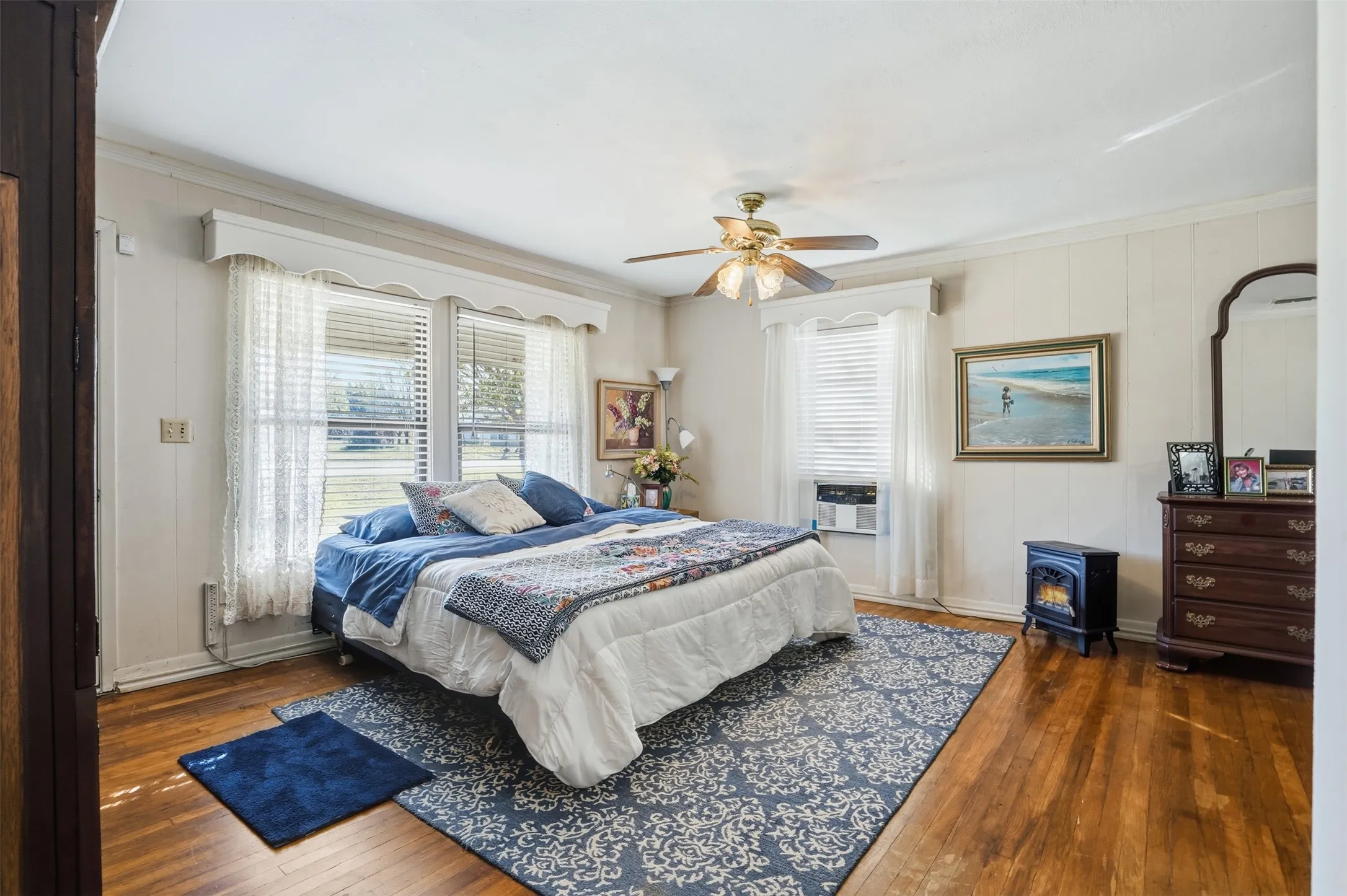 Bedroom featuring dark wood-style flooring, ornamental molding, ceiling fan, and a wood stove