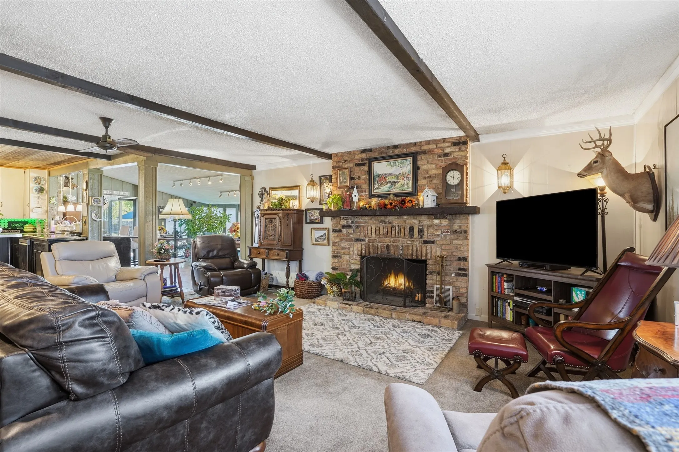 Living area featuring beamed ceiling, a textured ceiling, a fireplace, ceiling fan, and carpet floors