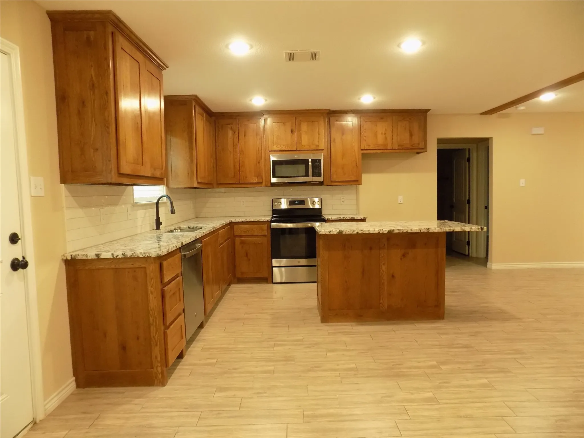 Kitchen featuring spacious cabinets, light granite countertops, appliances with stainless steel finishes, a kitchen island, and recessed lighting.
