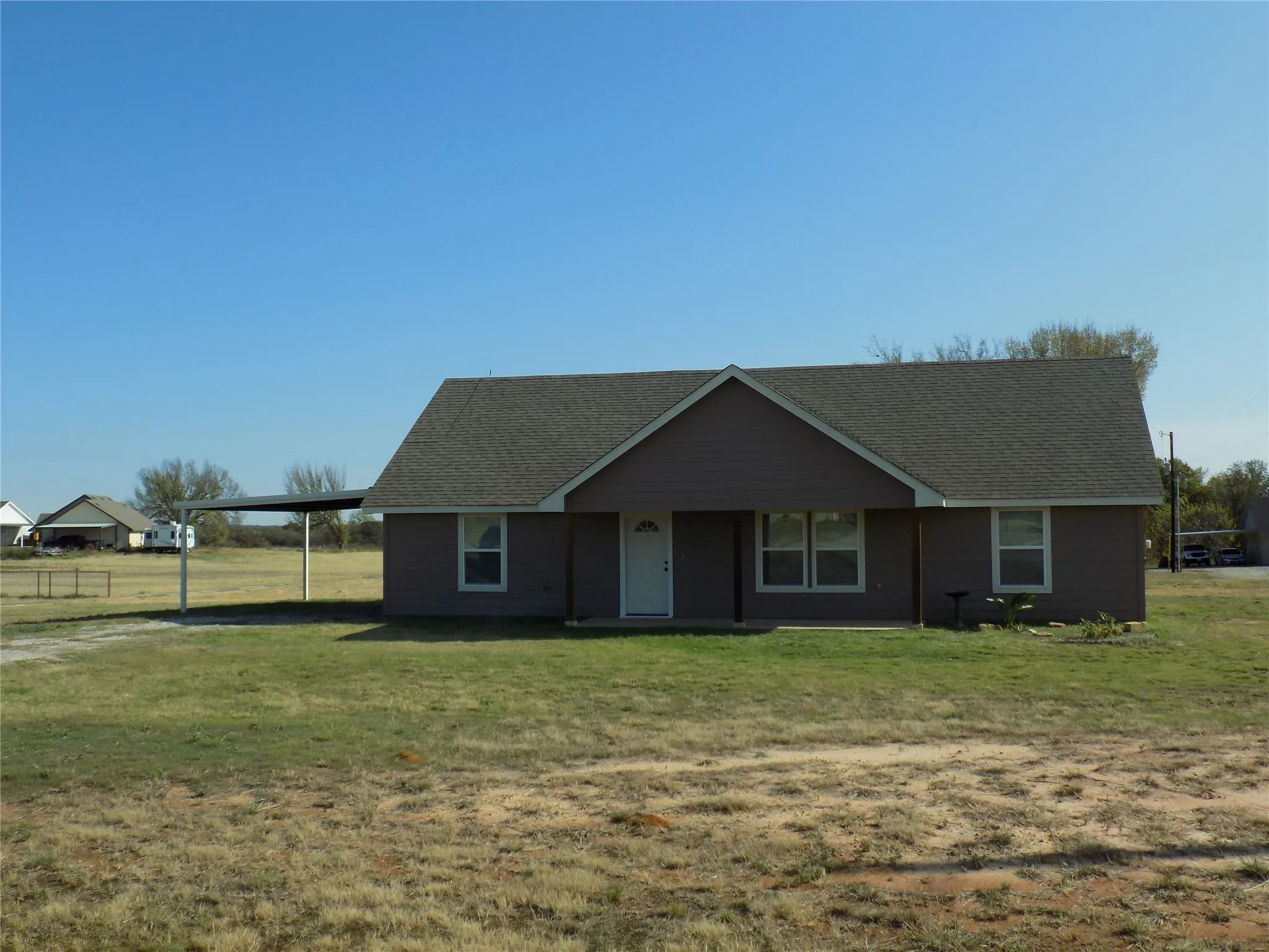 Single story home, with covered porch, an attached carport, and large front yard.