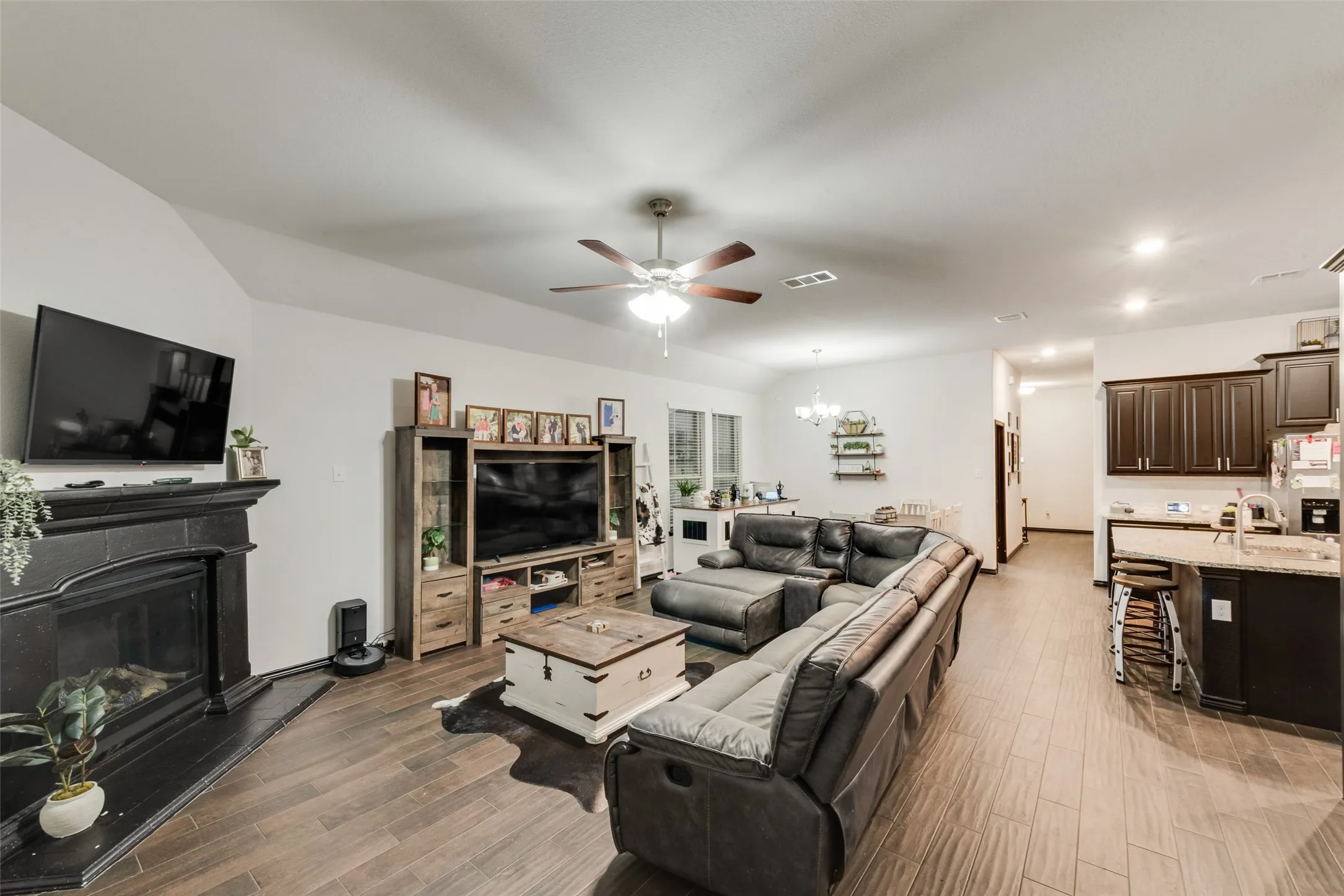 Living area with a chandelier, wood finish floors, ceiling fan, a glass covered fireplace, and recessed lighting