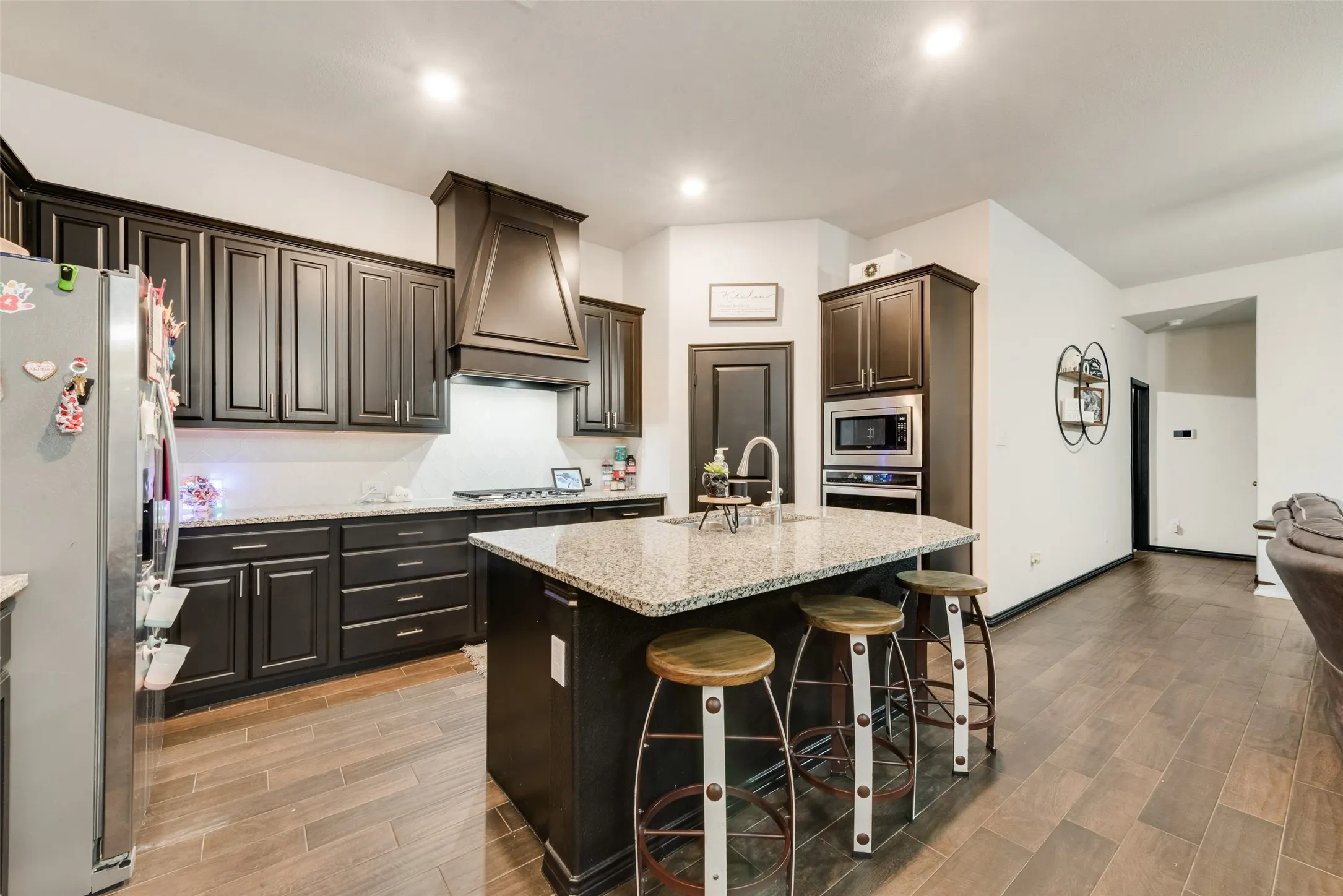 Kitchen with stainless steel appliances, a kitchen island with sink, wood finish floors, a breakfast bar, and light stone counters