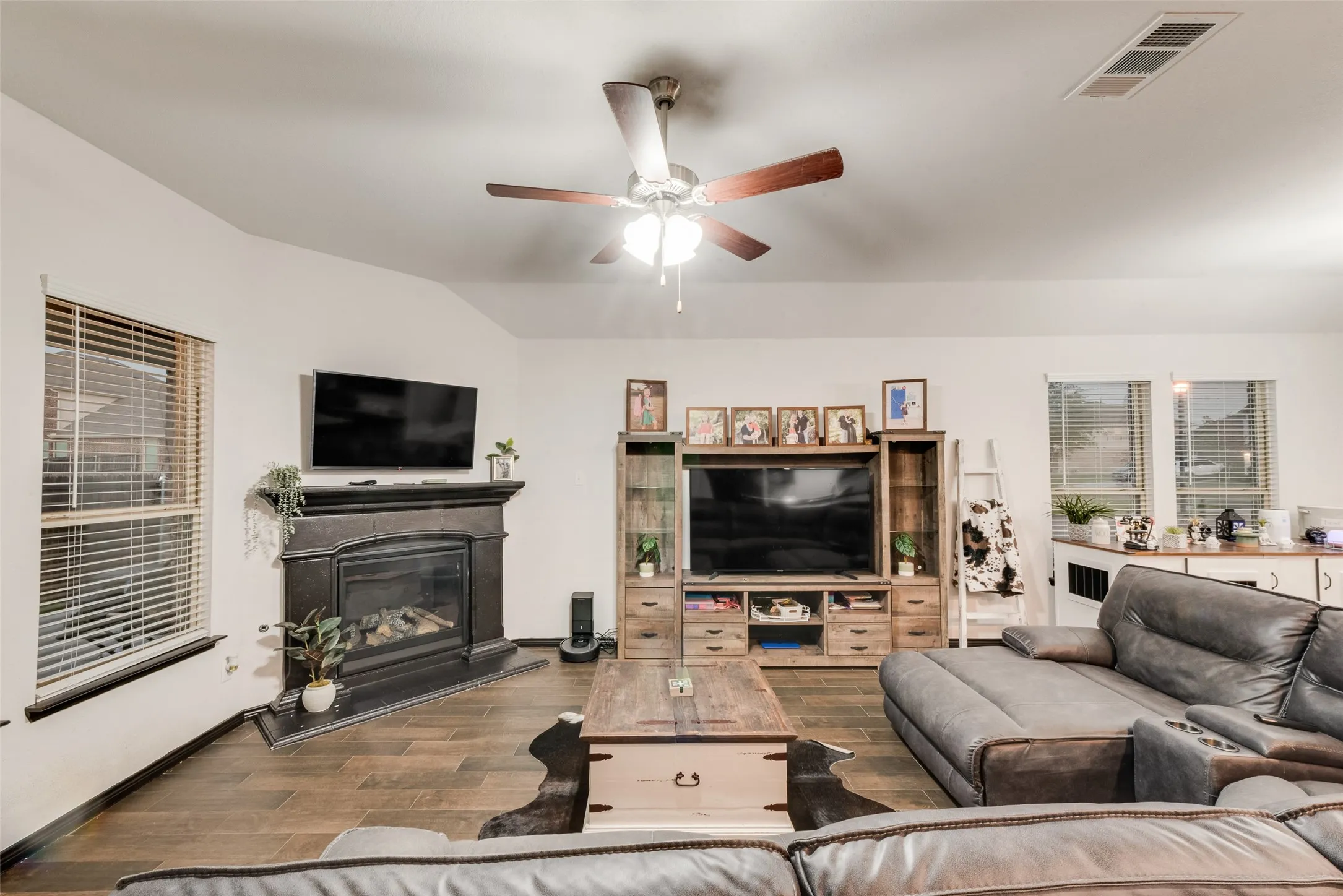 Living room with a glass covered fireplace, wood tiled floors, lofted ceiling, and ceiling fan