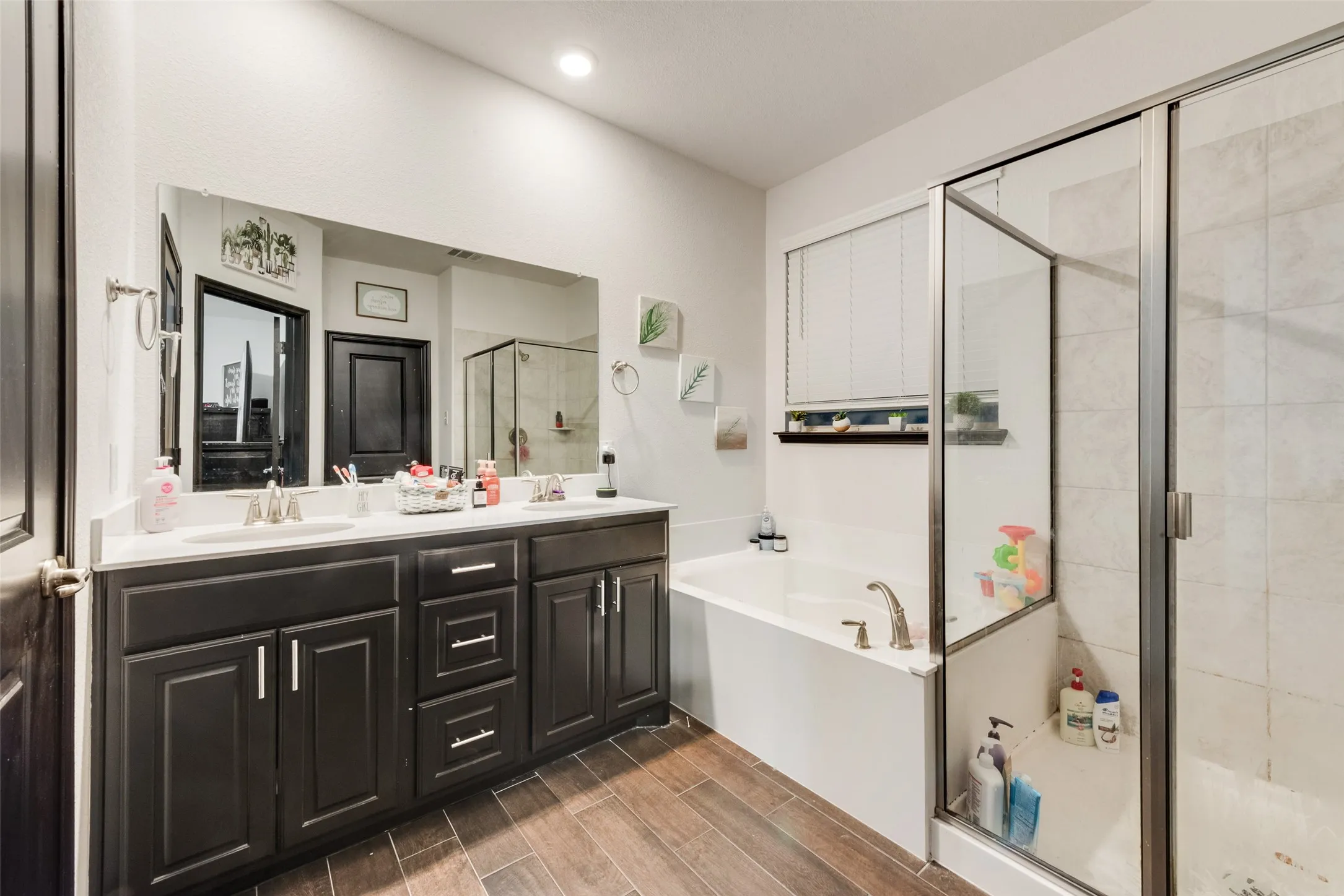 Full bathroom with a bath, double vanity, wood finish floors, and a stall shower