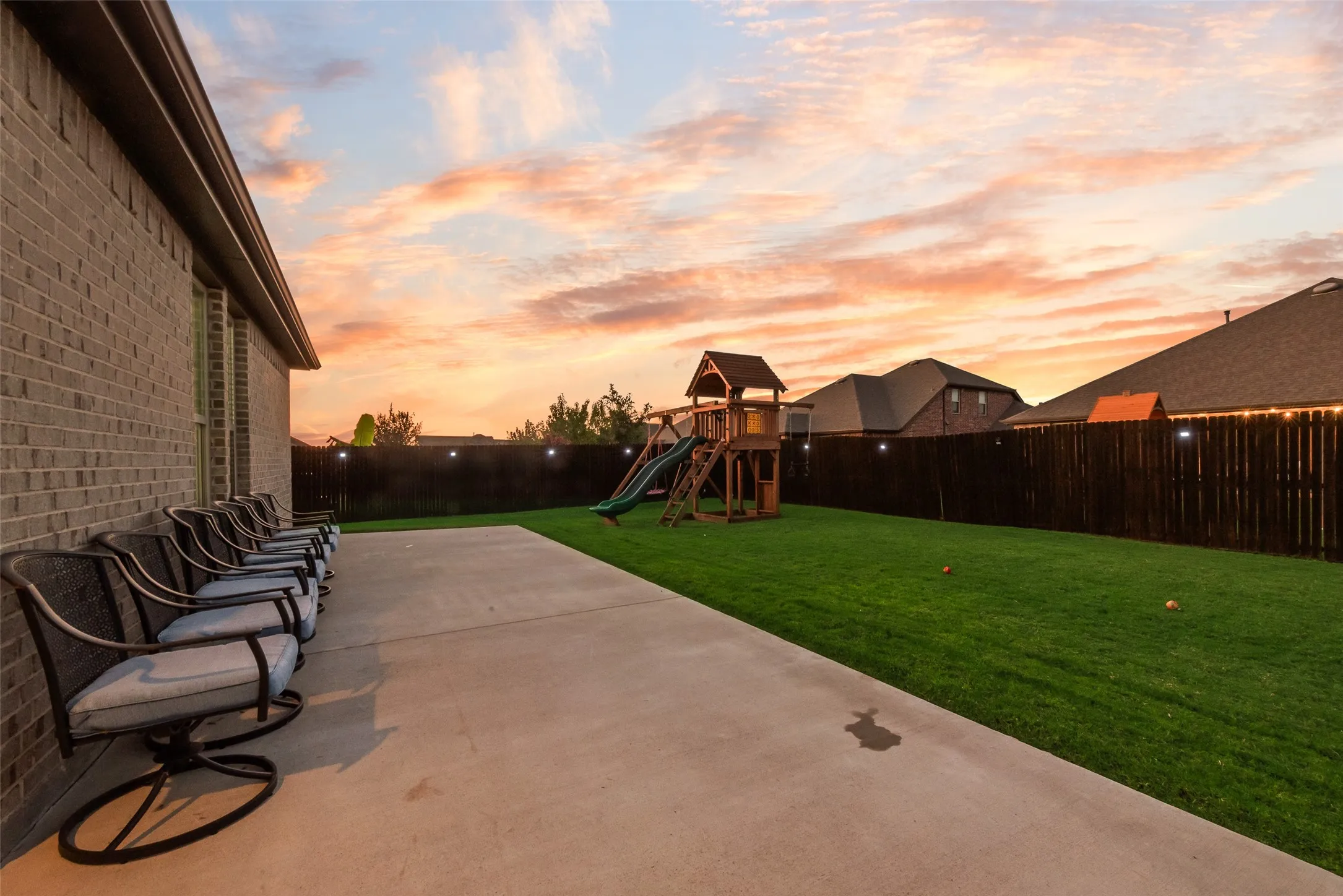 Patio terrace at dusk with a fenced backyard, a patio, and a playground