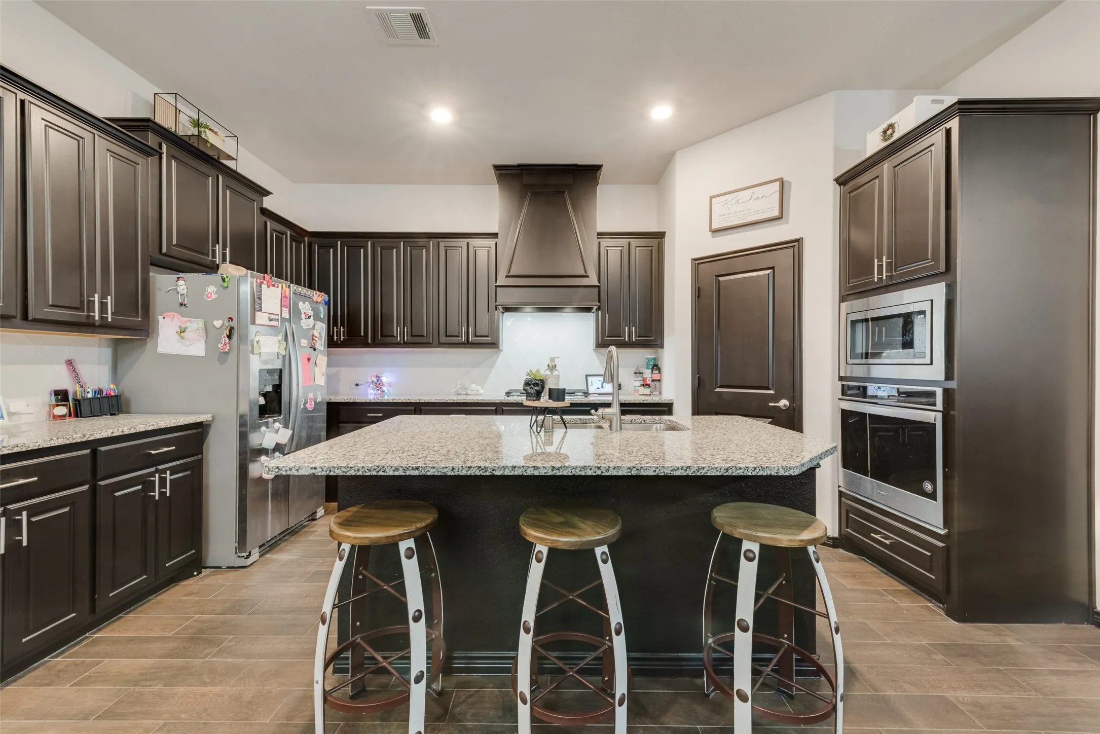 Kitchen with stainless steel appliances, a breakfast bar, a center island with sink, light stone counters, and premium range hood