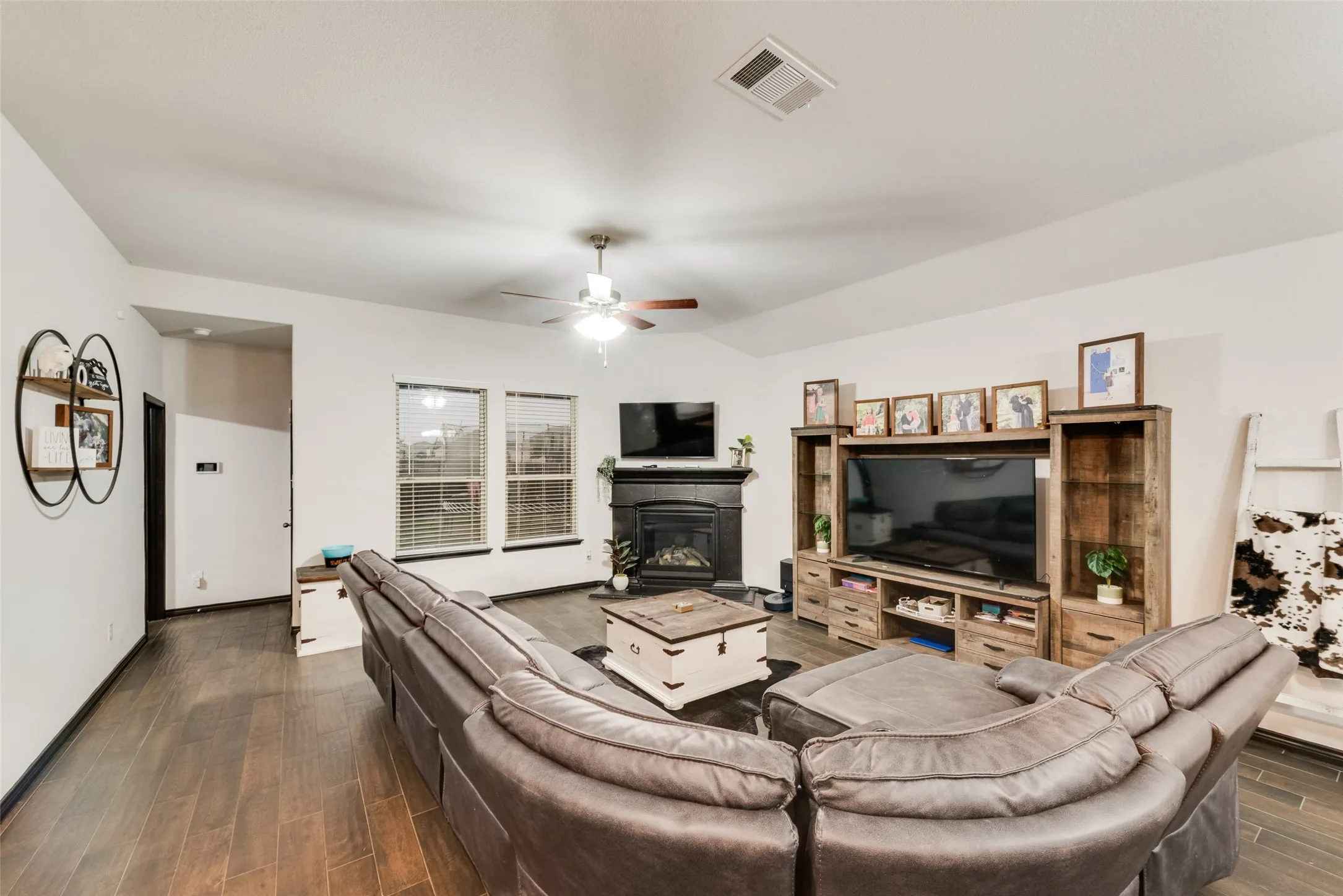 Living area with wood tiled floors, a glass covered fireplace, and a ceiling fan