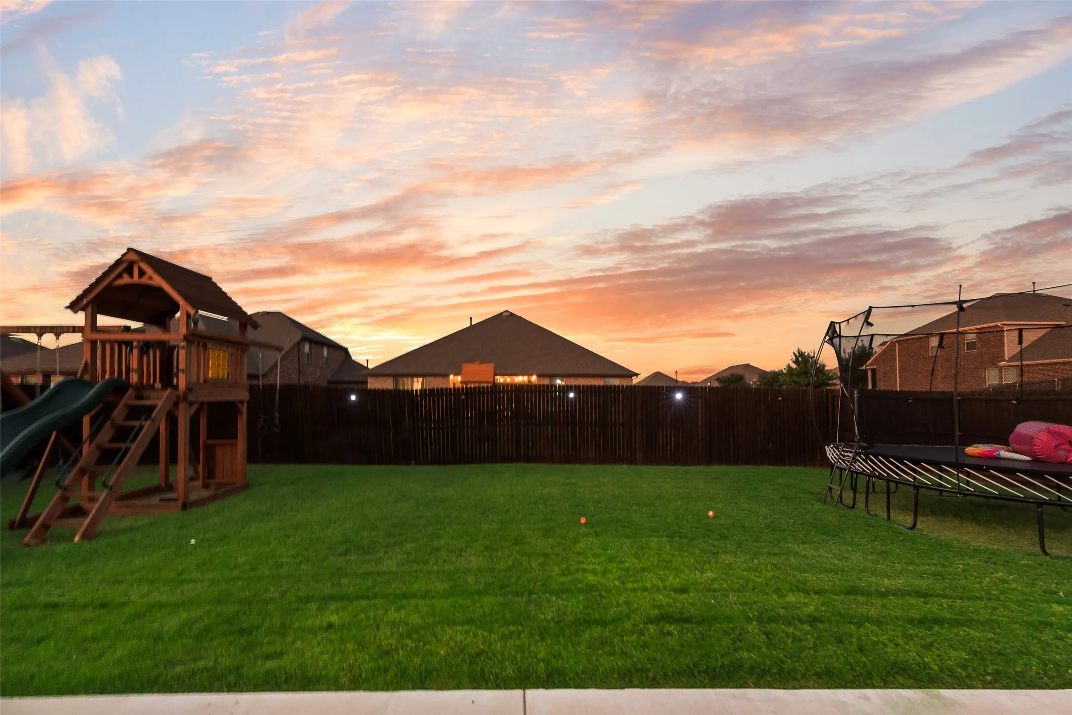 Yard at dusk with a fenced backyard, a trampoline, and a playground
