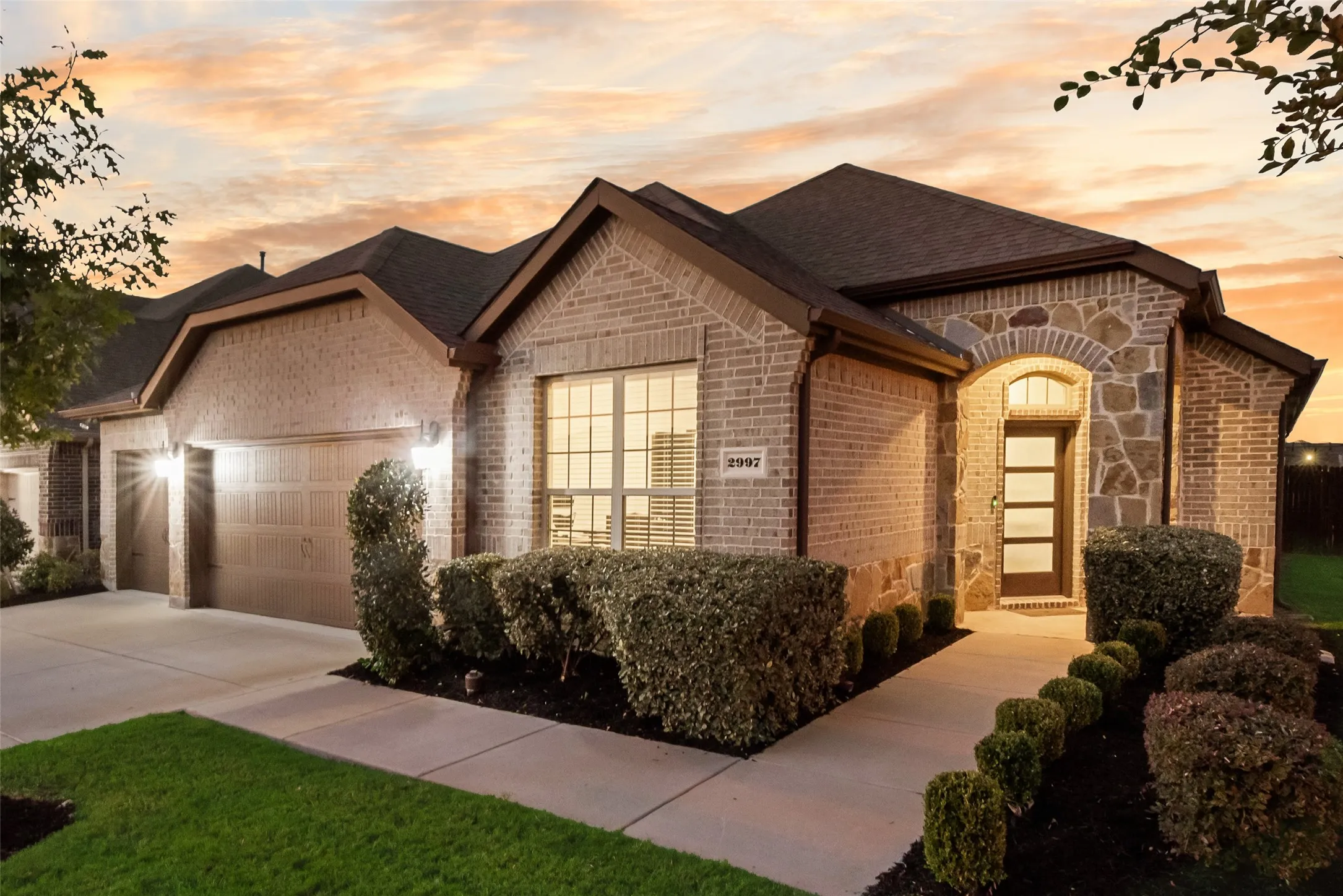 View of front of property with brick siding, stone siding, a garage, driveway, and roof with shingles