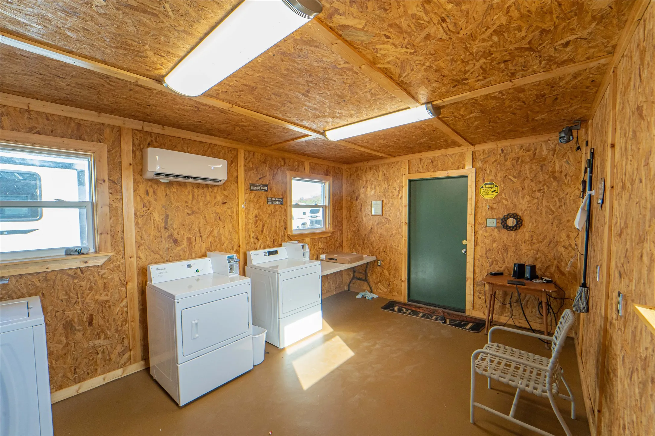 Community laundry room featuring concrete floors, washer and clothes dryer, a wall mounted AC, and wood walls