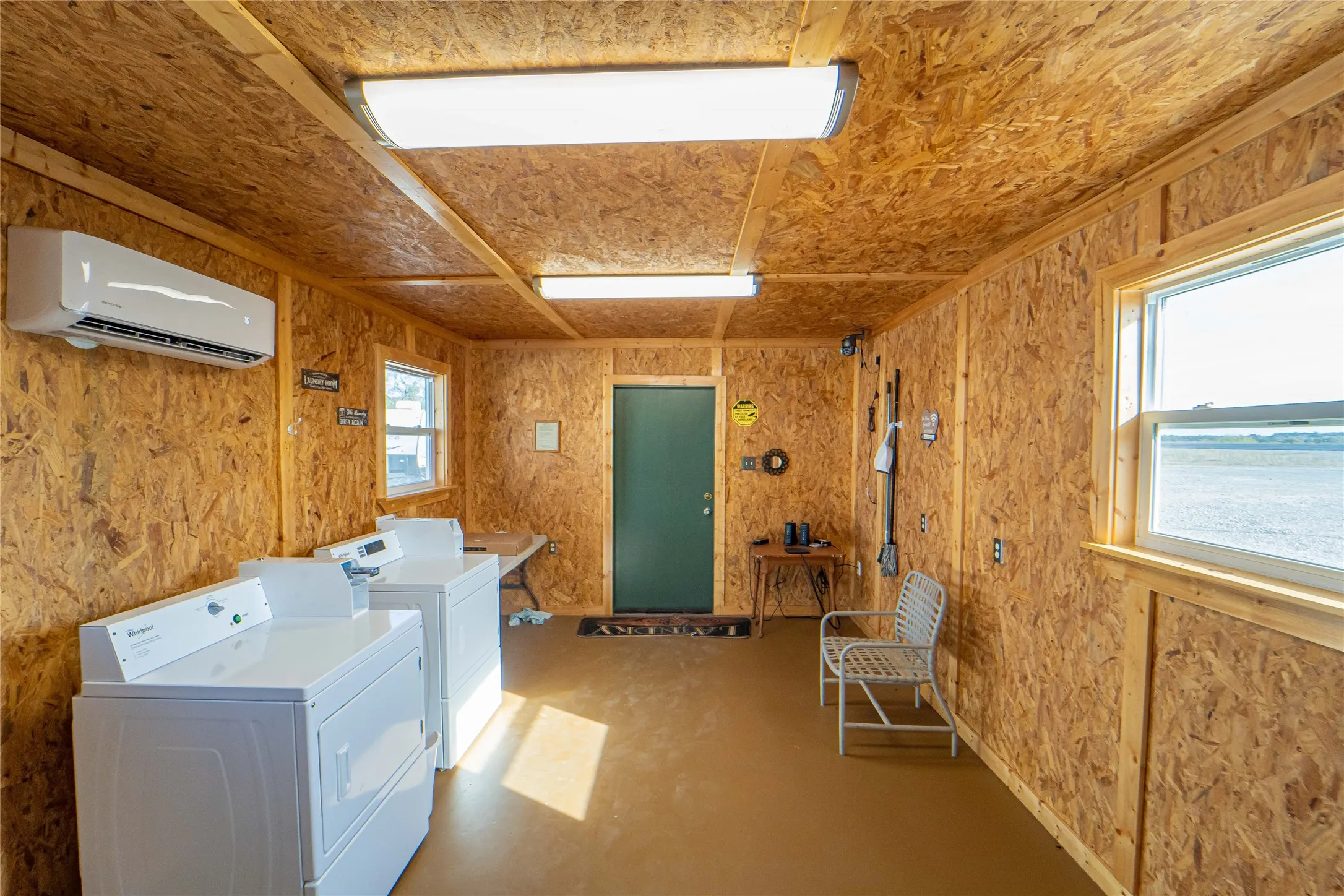 Shared laundry with a wall unit AC, wood walls, concrete floors, and washing machine and dryer