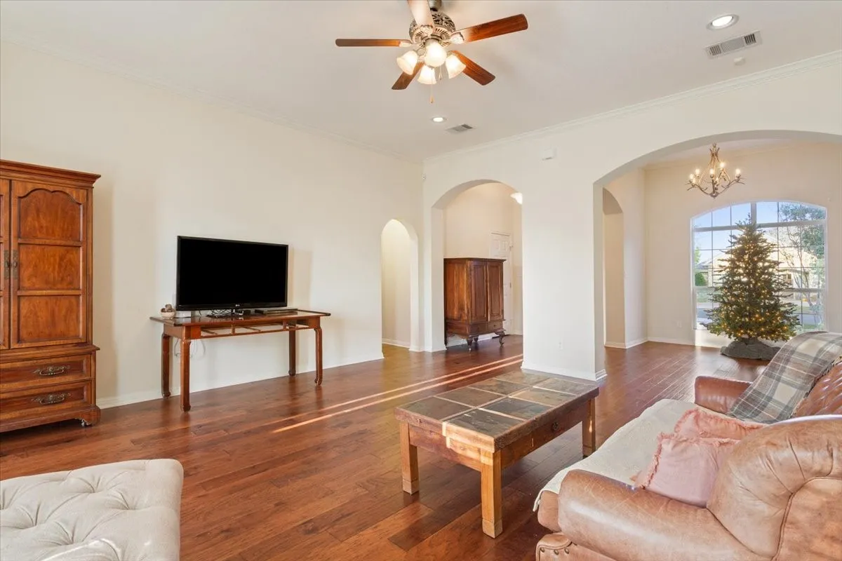 Living area with hardwood / wood-style flooring, arched walkways, crown molding, a chandelier, and a ceiling fan