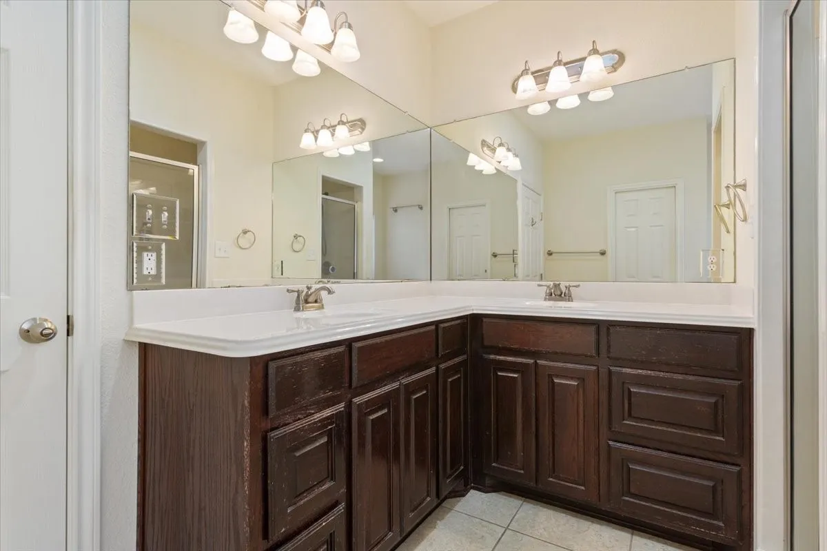 Full bathroom with double vanity, light tile patterned floors, and a shower stall