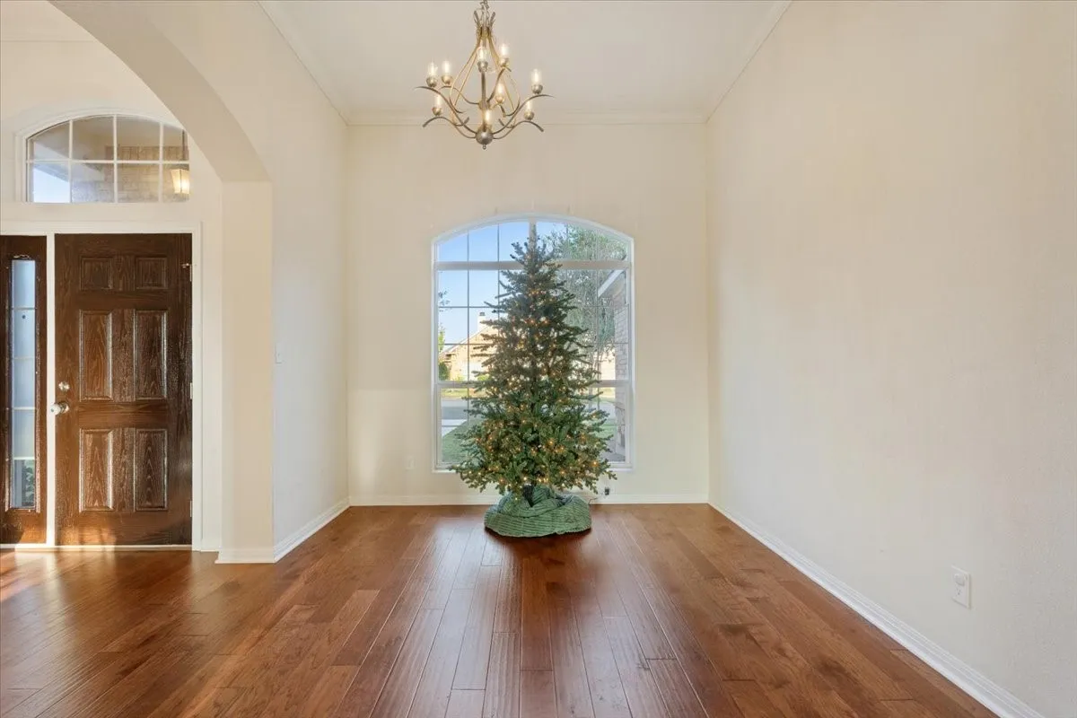 Entryway with a chandelier, arched walkways, crown molding, and wood-type flooring