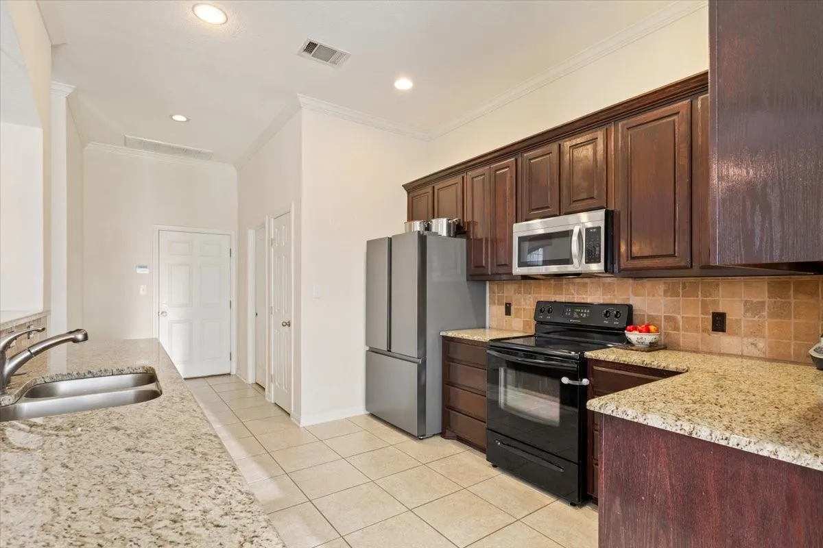 Kitchen with stainless steel appliances, crown molding, dark brown cabinets, light stone counters, and light tile patterned floors