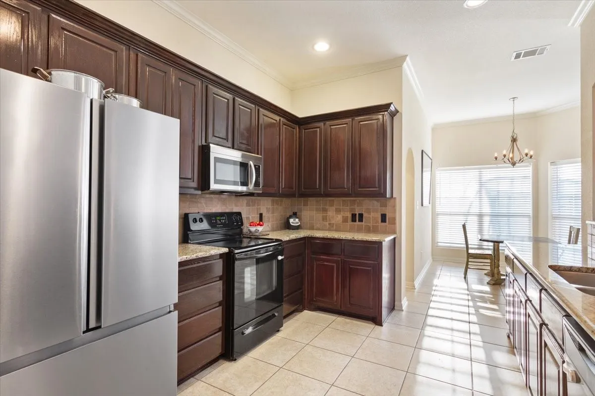Kitchen with appliances with stainless steel finishes, dark brown cabinets, hanging light fixtures, crown molding, and light stone counters