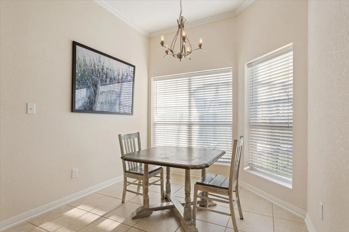 Dining room featuring light tile patterned floors, a chandelier, plenty of natural light, a textured wall, and crown molding