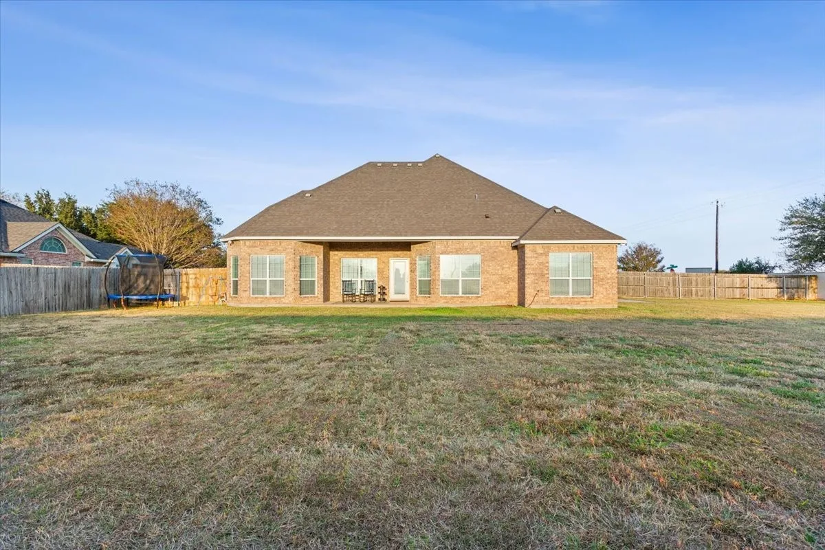 Back of property with a fenced backyard, a patio area, a trampoline, brick siding, and a shingled roof