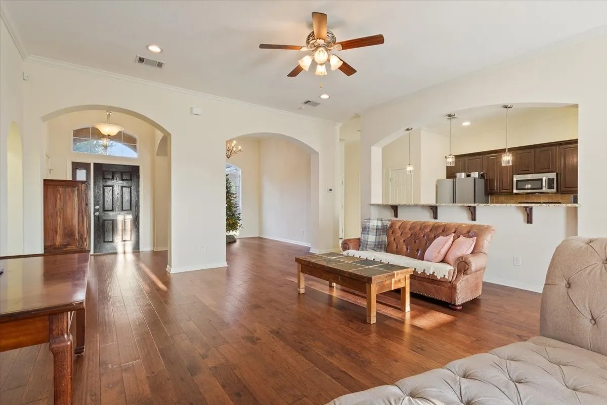 Living room with crown molding, arched walkways, dark wood finished floors, a ceiling fan, and recessed lighting