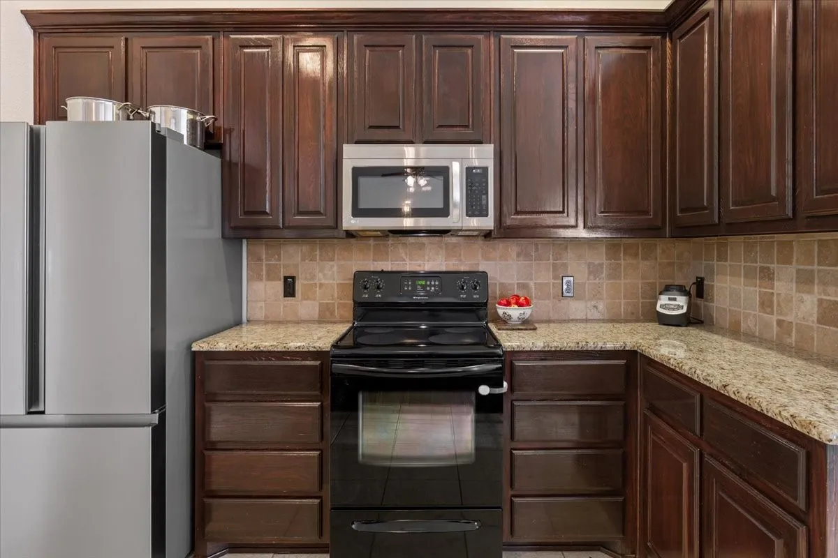 Kitchen featuring stainless steel appliances, dark brown cabinetry, light stone counters, and tasteful backsplash