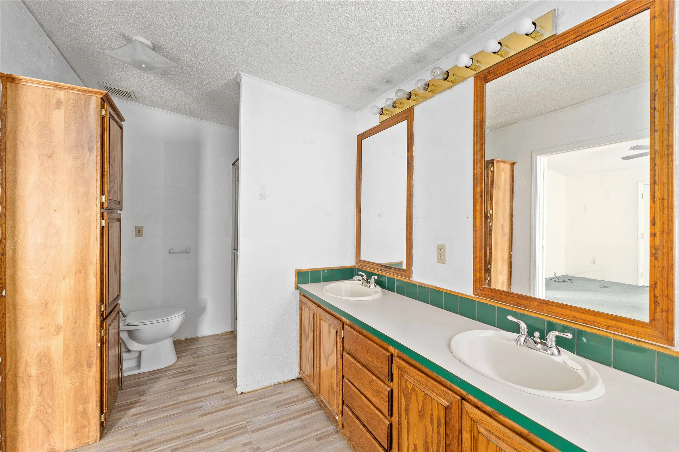 Full bathroom featuring a textured ceiling, double vanity, and light wood-type flooring