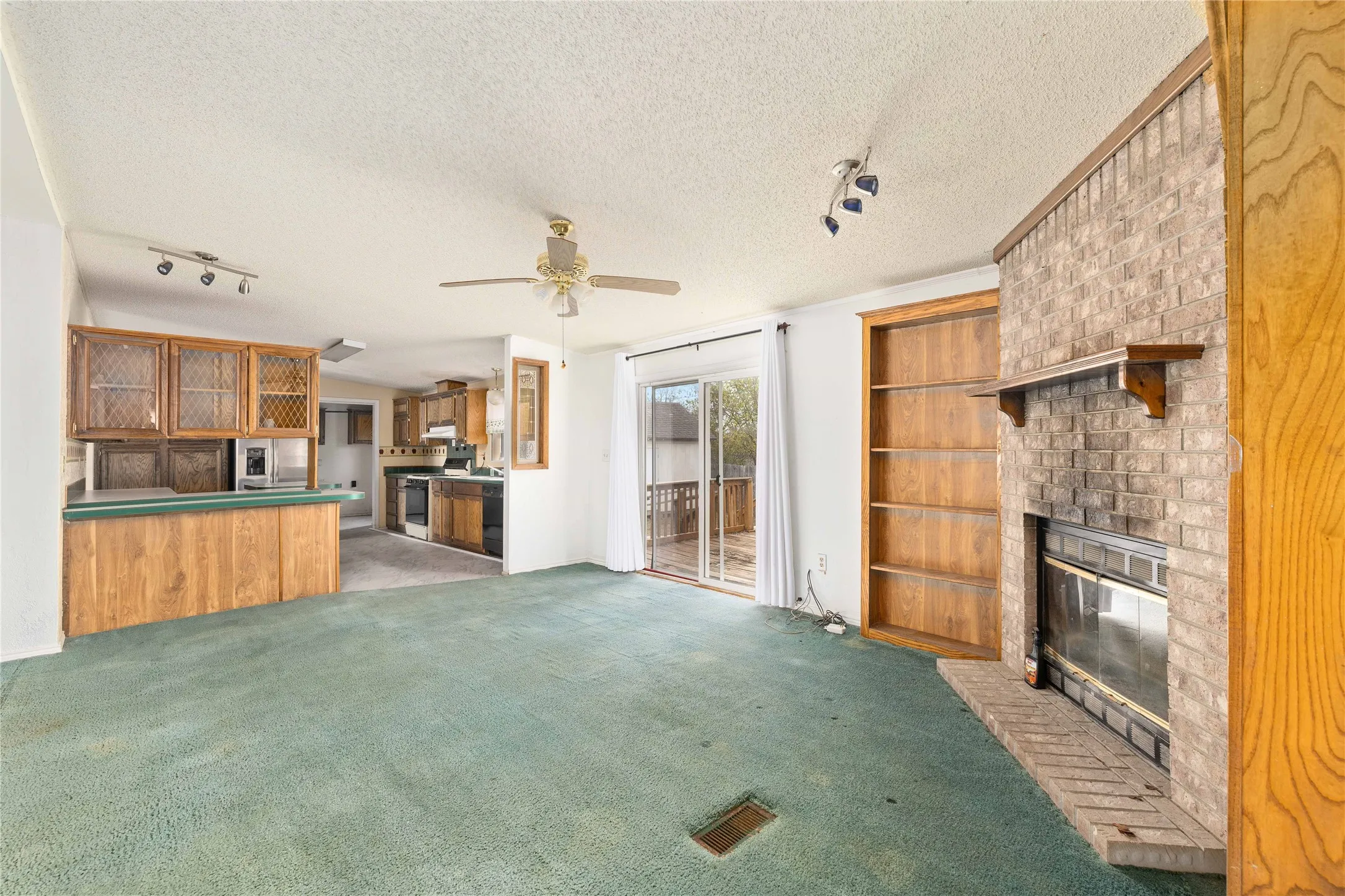 Unfurnished living room with track lighting, a textured ceiling, a fireplace, carpet flooring, and a ceiling fan