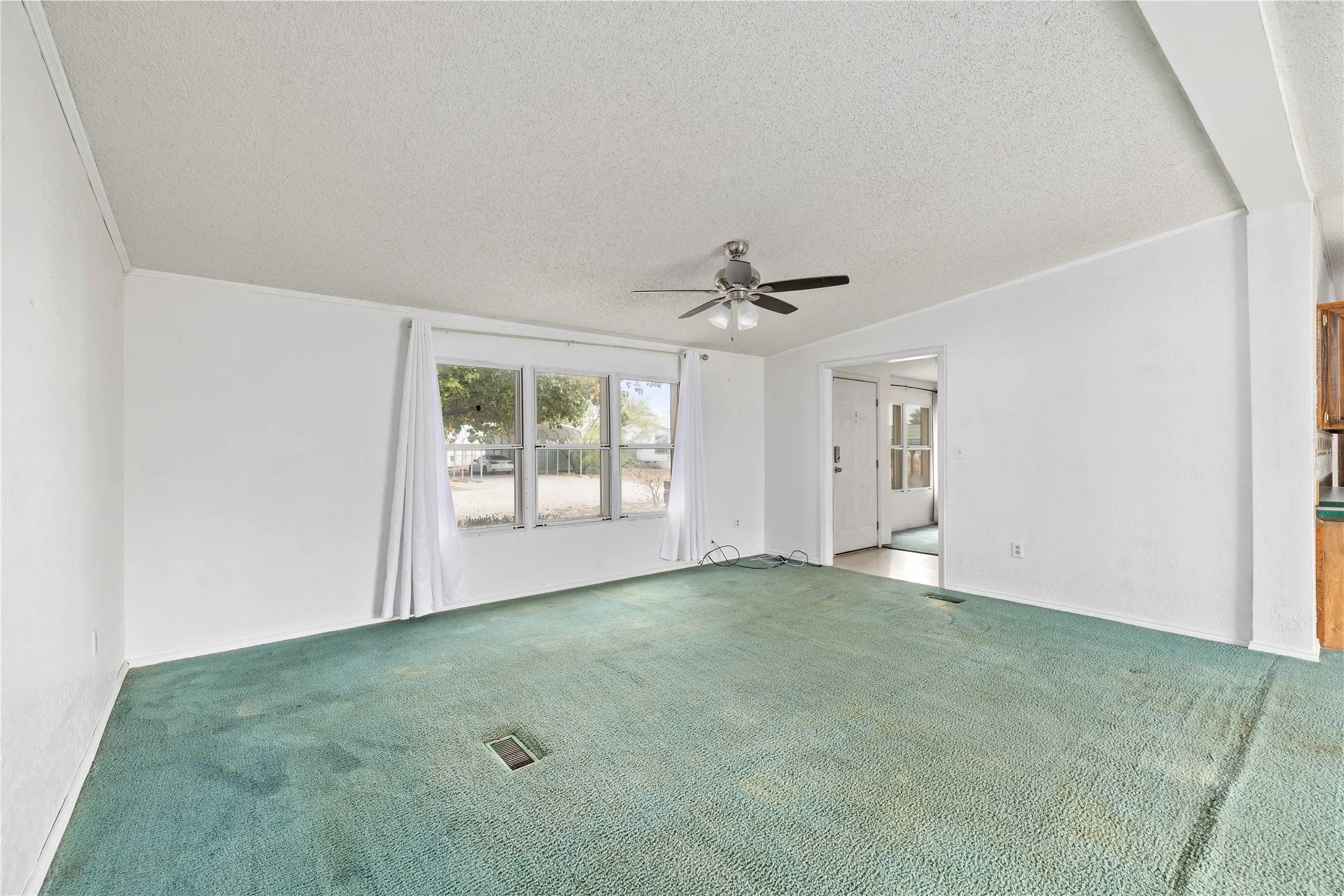 Empty room featuring a textured ceiling, carpet, and a ceiling fan