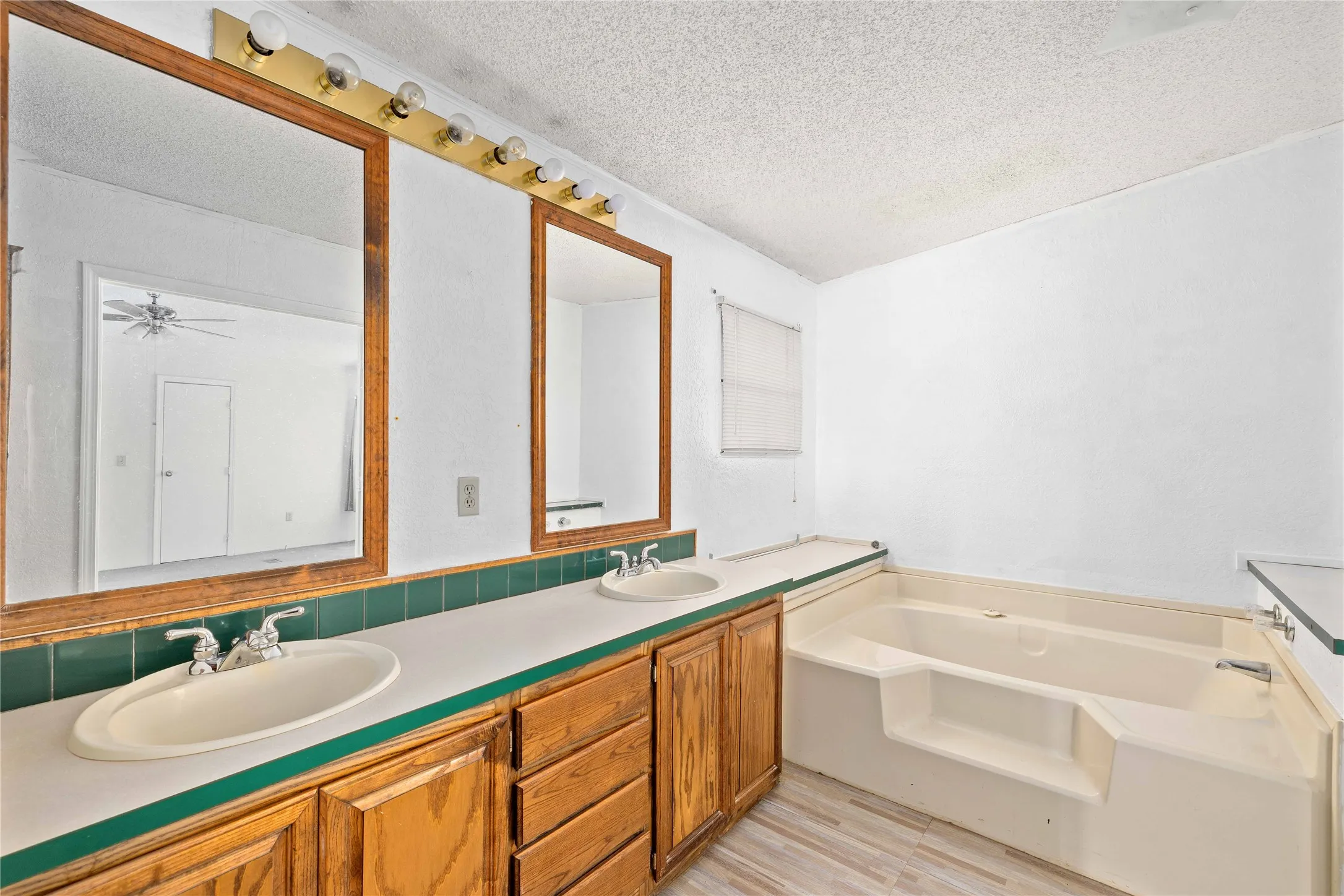 Full bath with double vanity, a textured ceiling, a garden tub, and light wood-style flooring