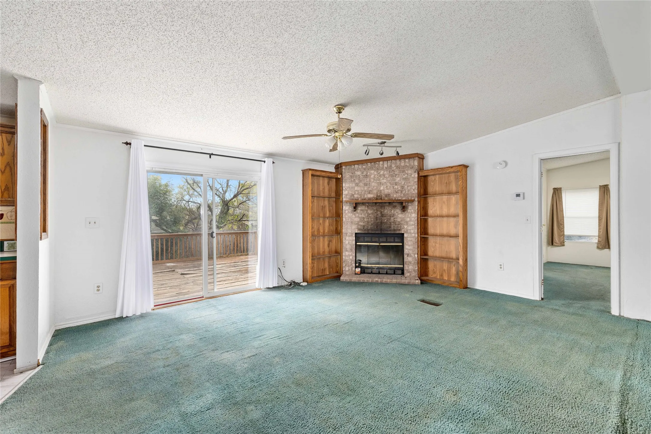 Unfurnished living room featuring a textured ceiling, carpet, a brick fireplace, and a ceiling fan