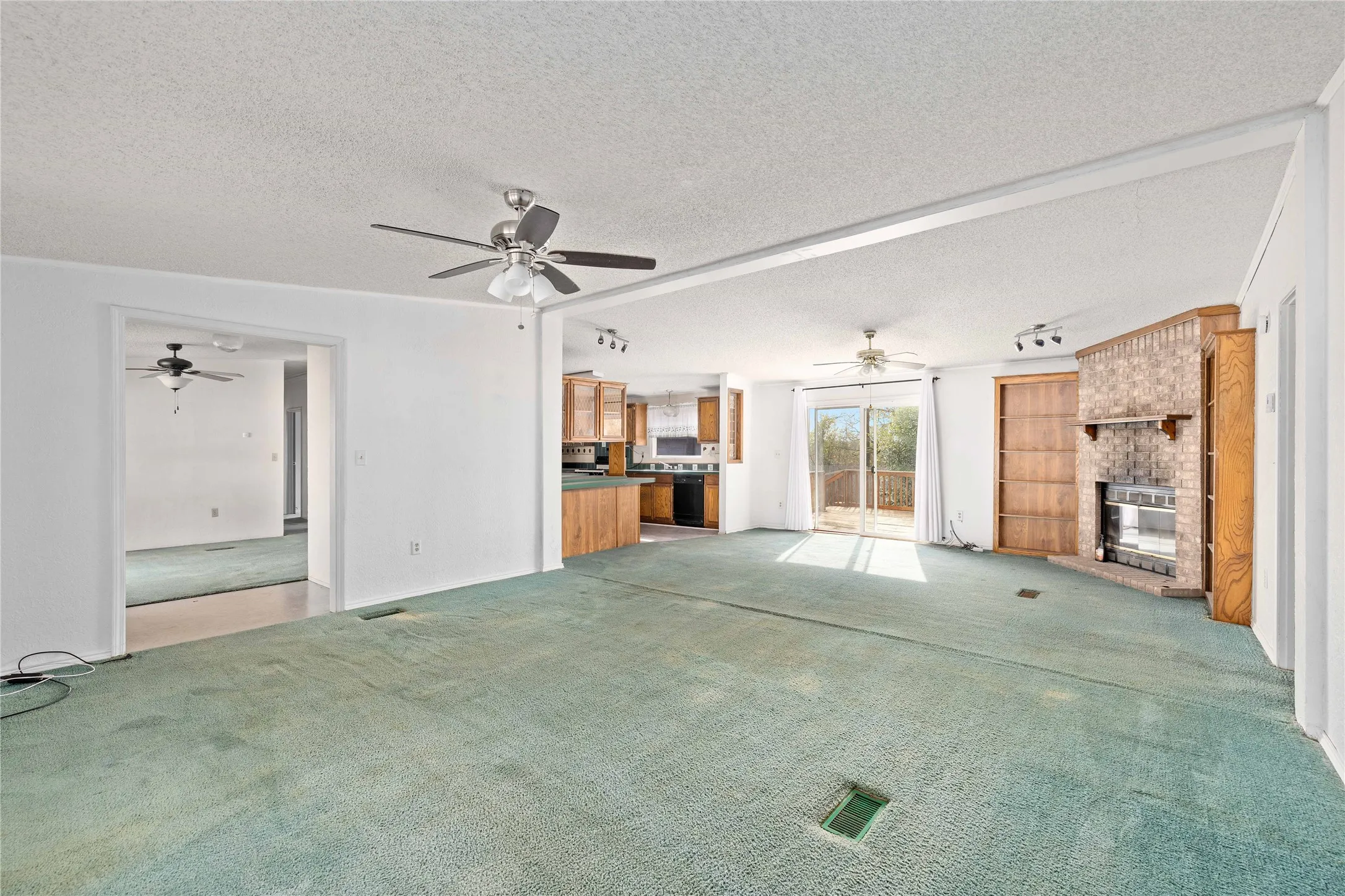 Unfurnished living room featuring carpet floors, a brick fireplace, a textured ceiling, a ceiling fan, and track lighting