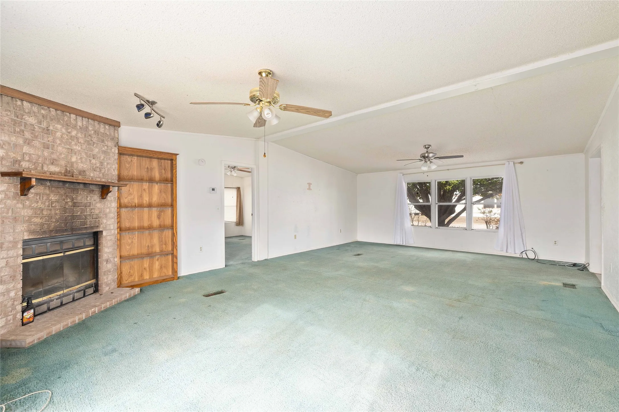 Unfurnished living room with carpet, a brick fireplace, ceiling fan, lofted ceiling, and a textured ceiling