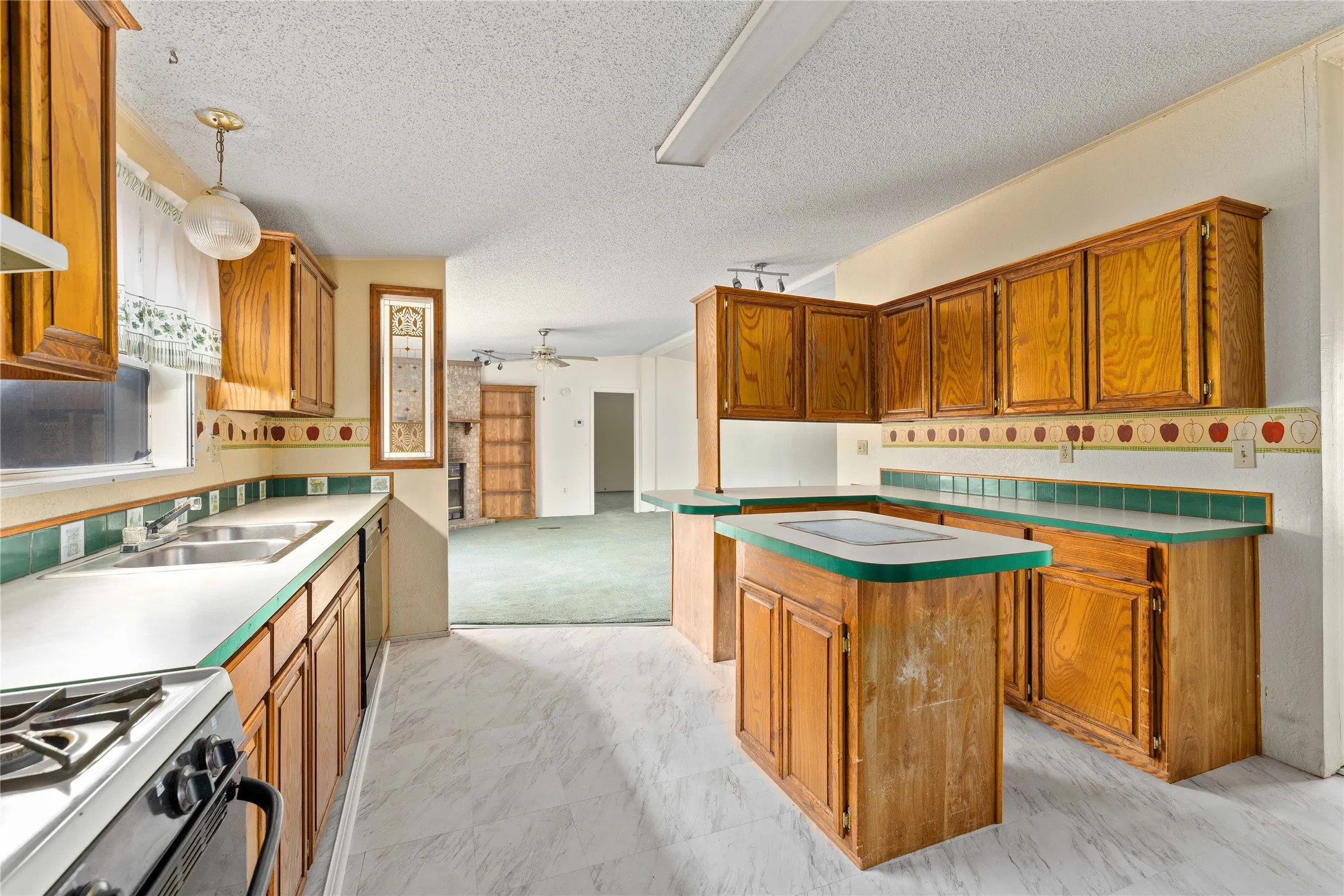 Kitchen with brown cabinets, range with gas stovetop, decorative light fixtures, ceiling fan, and a textured ceiling