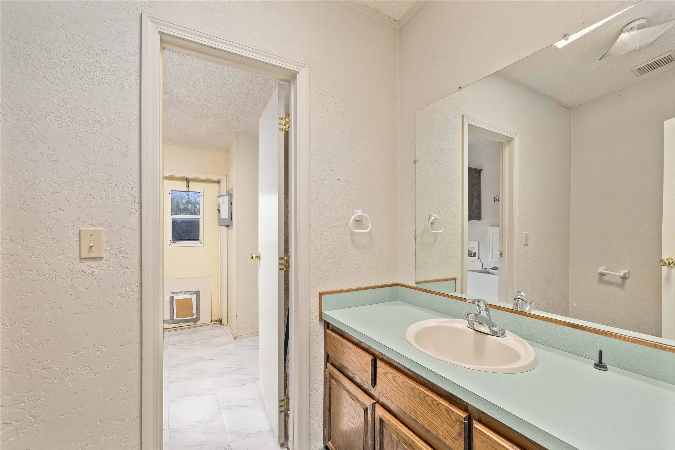 Half bathroom with a textured wall, light marble finish floors, and vanity
