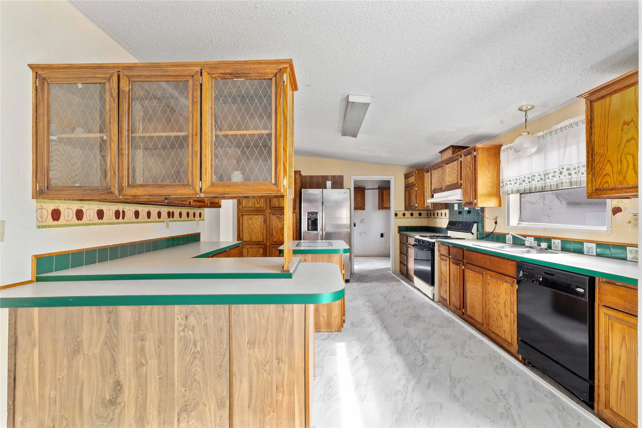 Kitchen featuring brown cabinetry, light countertops, range with gas stovetop, vaulted ceiling, and a textured ceiling