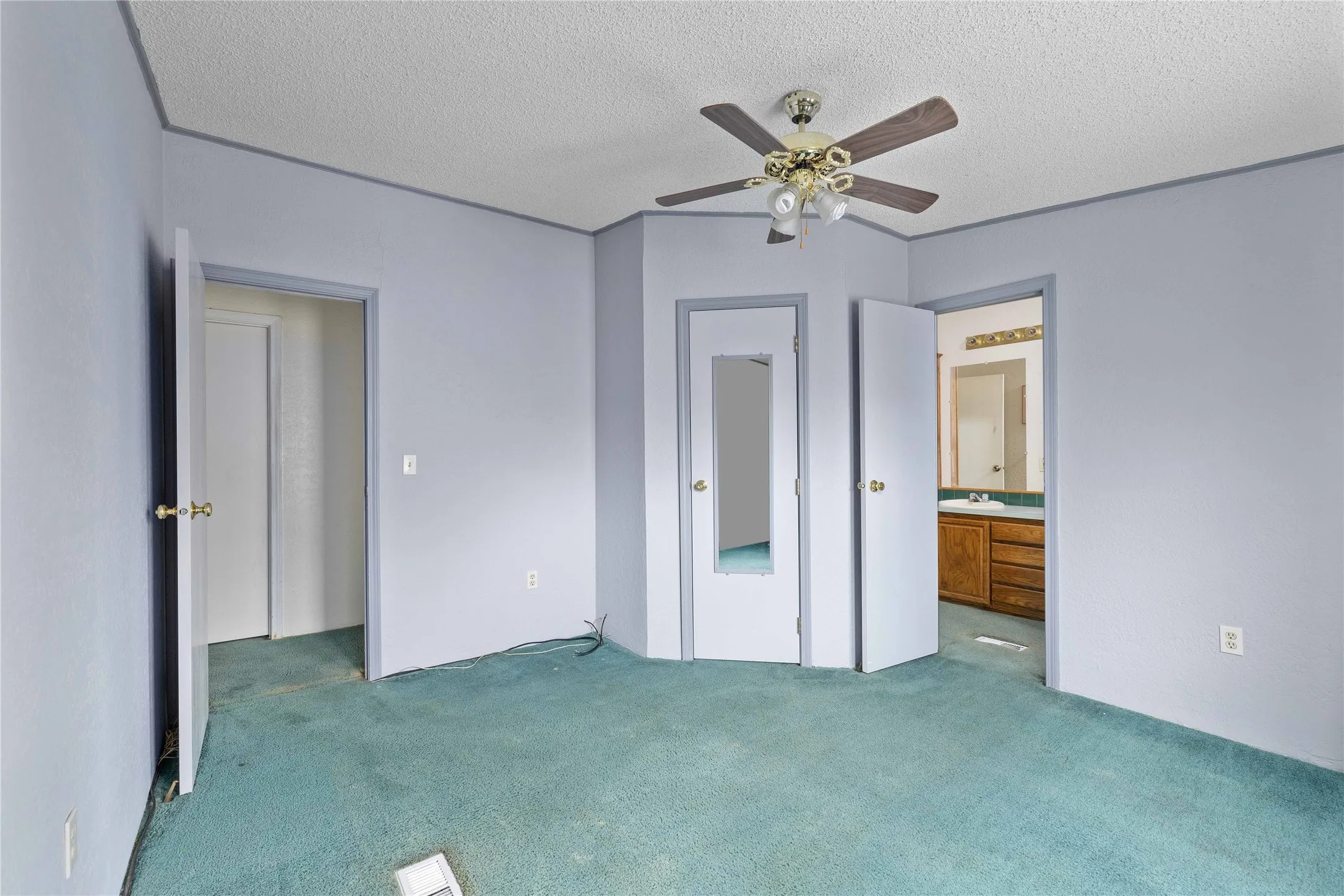 Unfurnished bedroom with a textured ceiling, carpet flooring, ensuite bathroom, and a ceiling fan