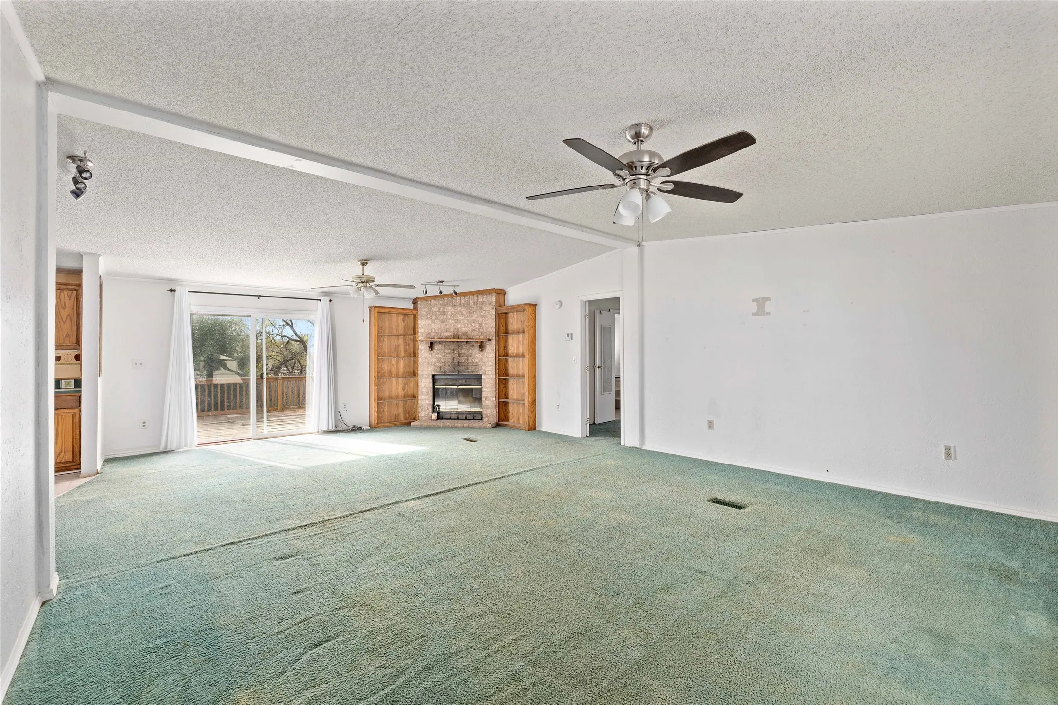 Unfurnished living room with carpet flooring, vaulted ceiling, a large fireplace, a textured ceiling, and ceiling fan