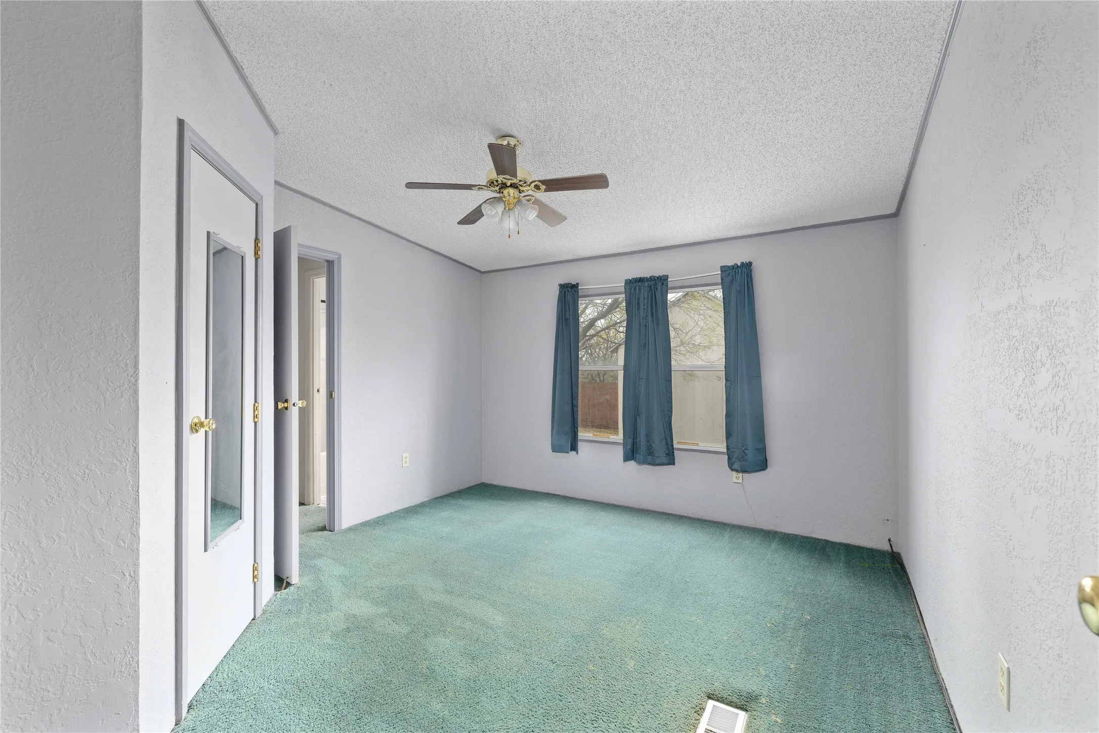 Empty room featuring a textured wall, carpet floors, a textured ceiling, and ceiling fan